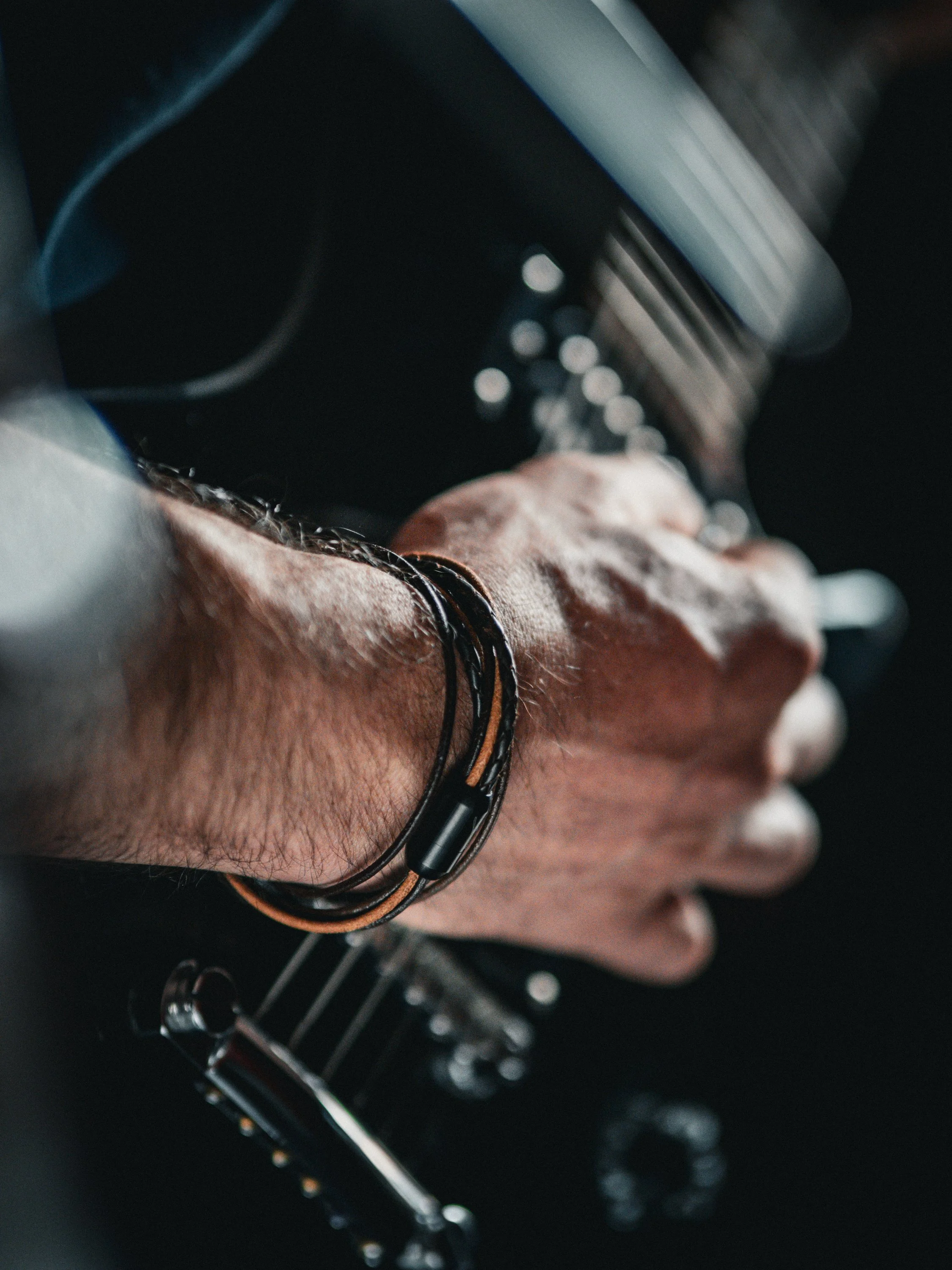 Nahaufnahme einer Hand, die ein Motorrad hält, mit Lederarmband und im Hintergrund ein Tachometer.