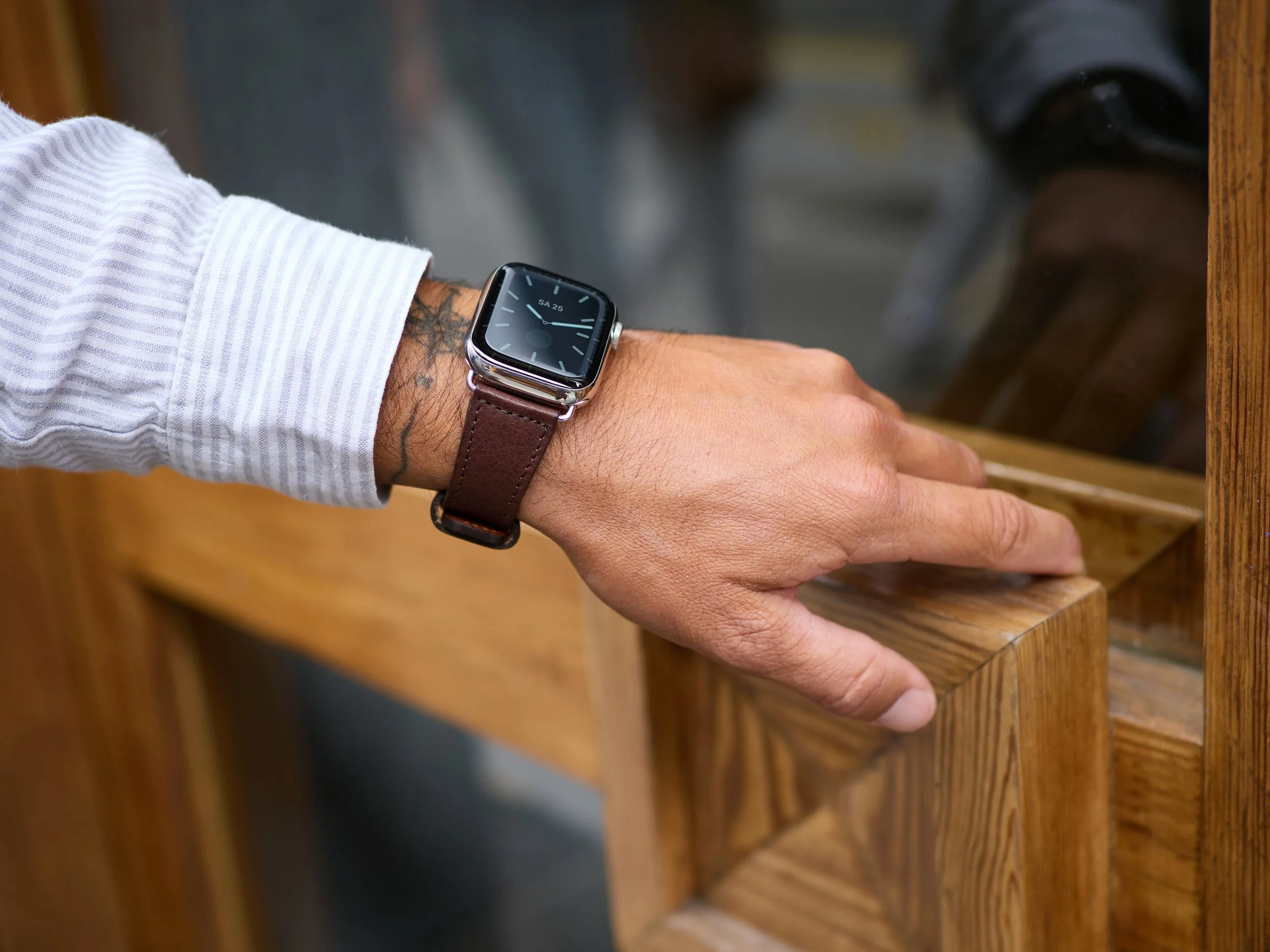 Hand mit Armbanduhr, die auf einer Holzfensterbank ruht.