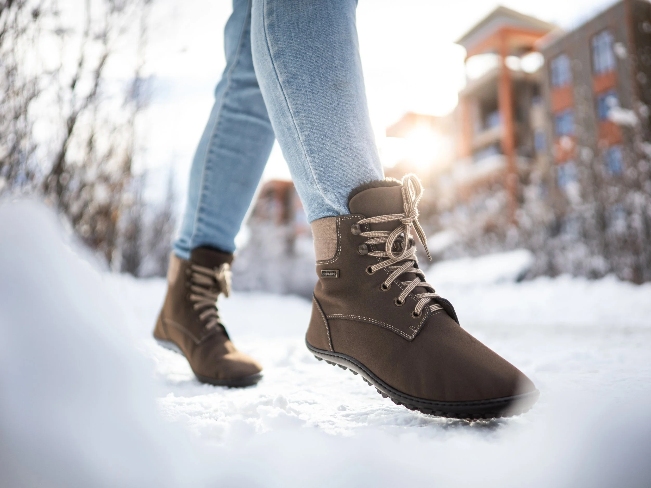 Nahaufnahme von robuste Schneestiefel, getragen von einer Person mit blauen Jeans, im Schnee bei Sonnenuntergang