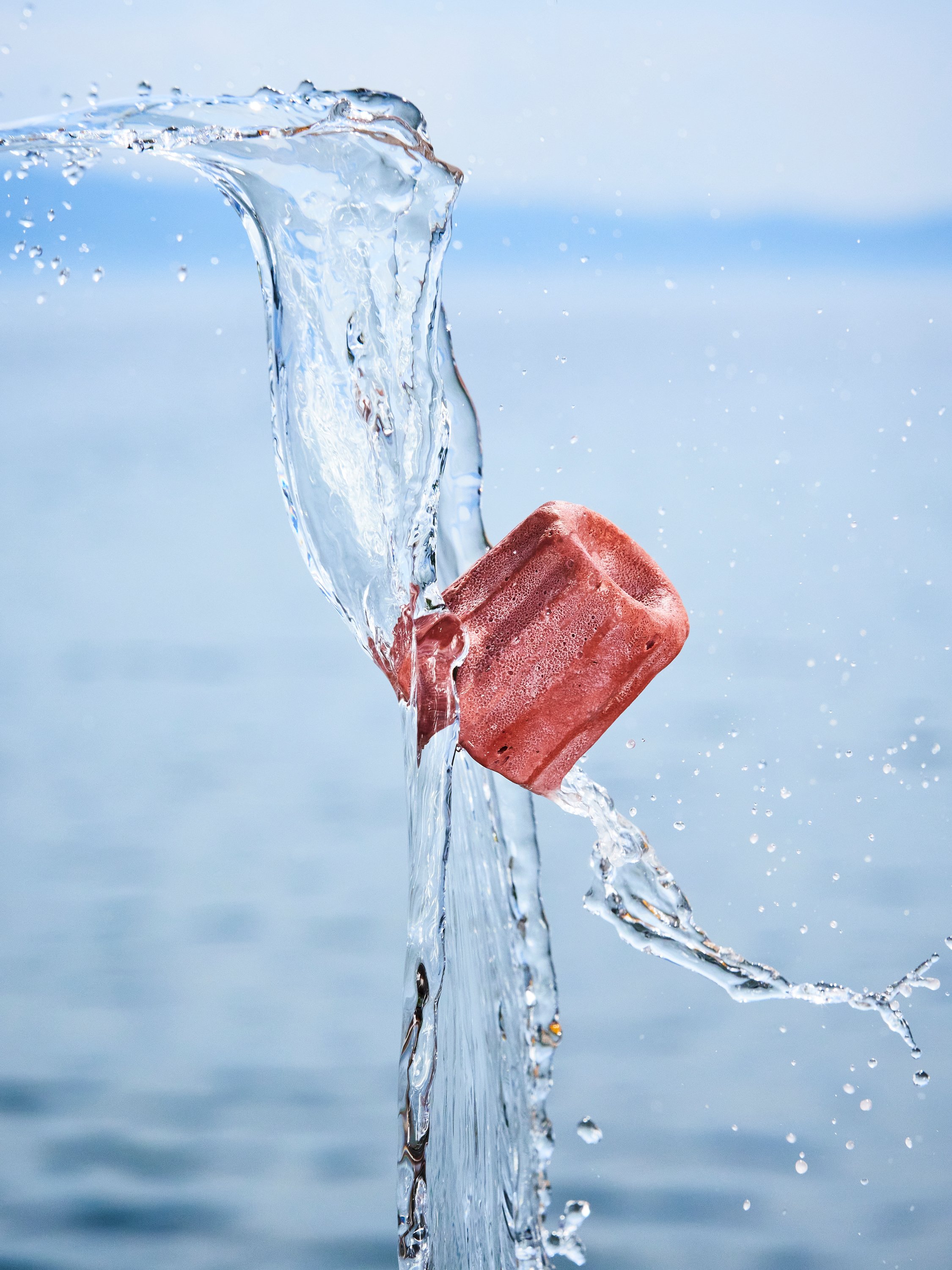 Ein roter Eisklump taucht in Wasser ein, Wasser spritzt auf.