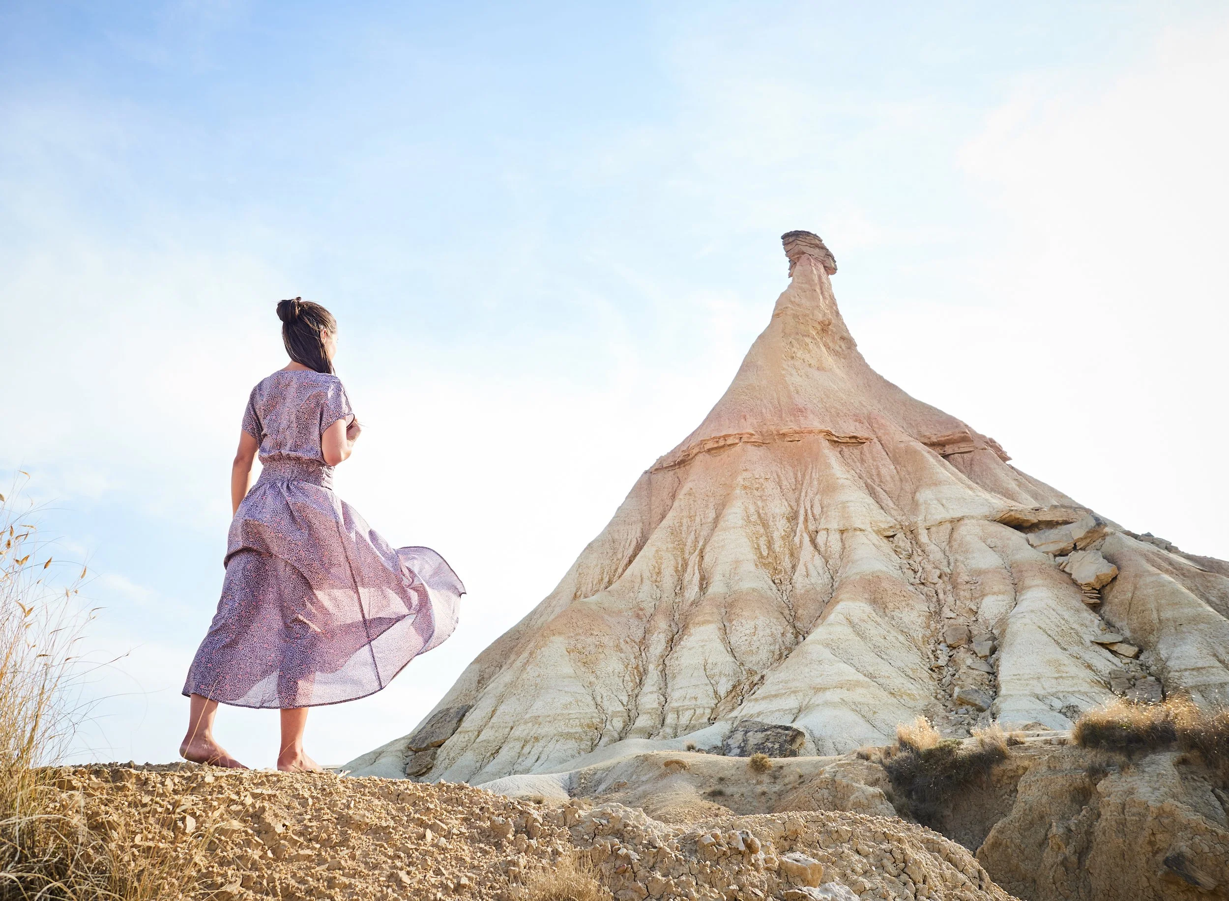 Eine Frau in einem hübschen Kleid steht auf einer Erdhügel und schaut auf eine einzigartige, pyramidenartige Felsformation in der Wüste bei Sonnenaufgang oder Sonnenuntergang.