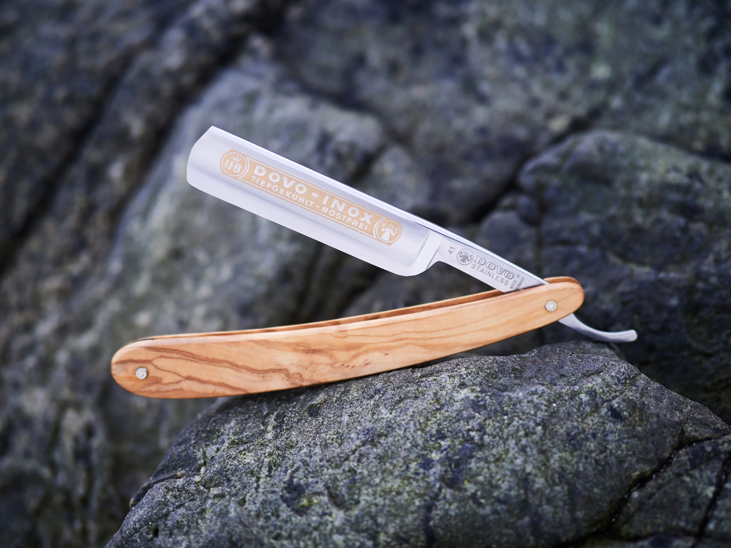 Rasiermesser mit holzartigem Griff und Edelstahlklinge, liegt auf schwarzen Felsen