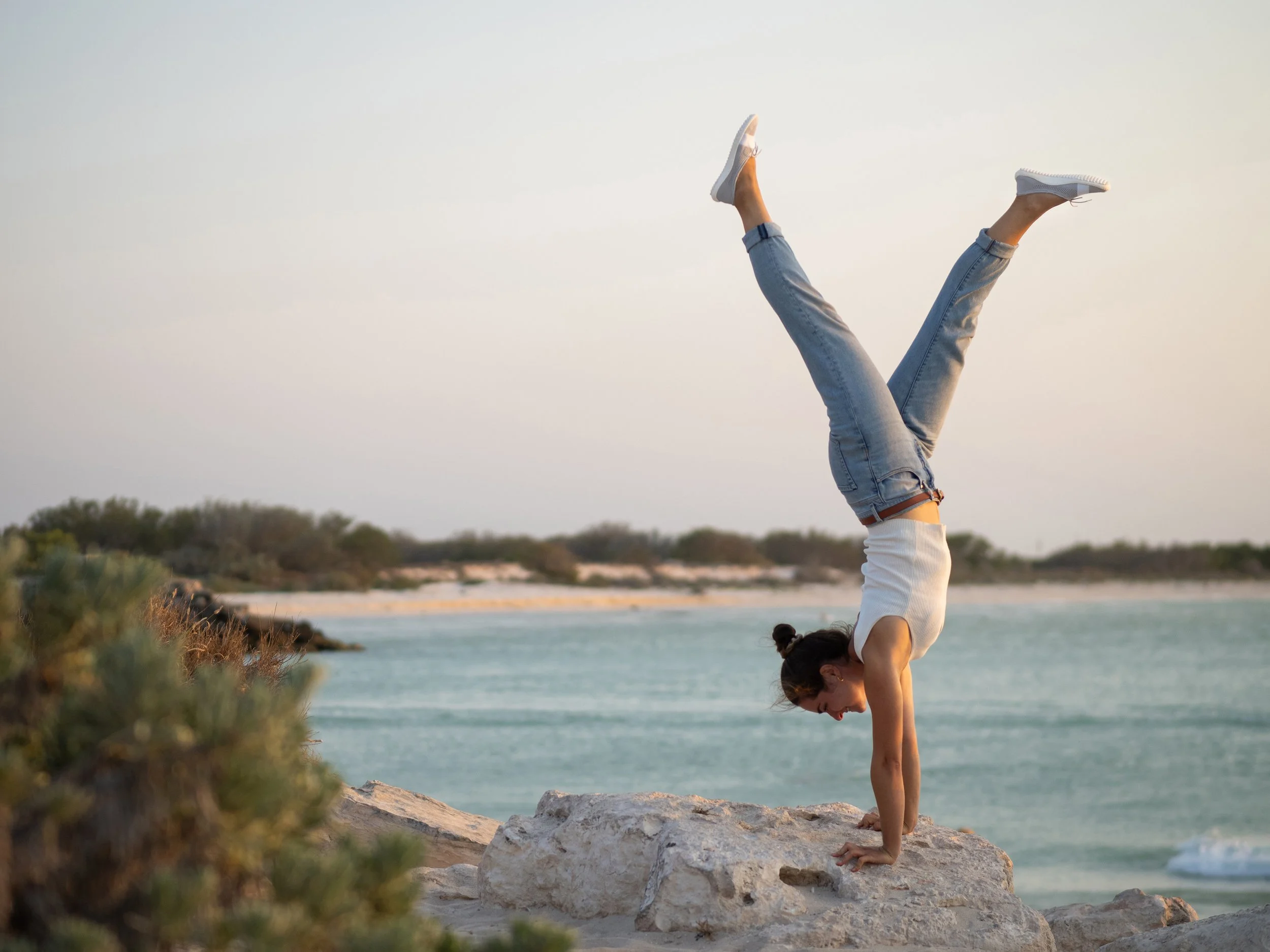 Frau macht Handstand auf einem Felsen am Strand bei Sonnenuntergang.