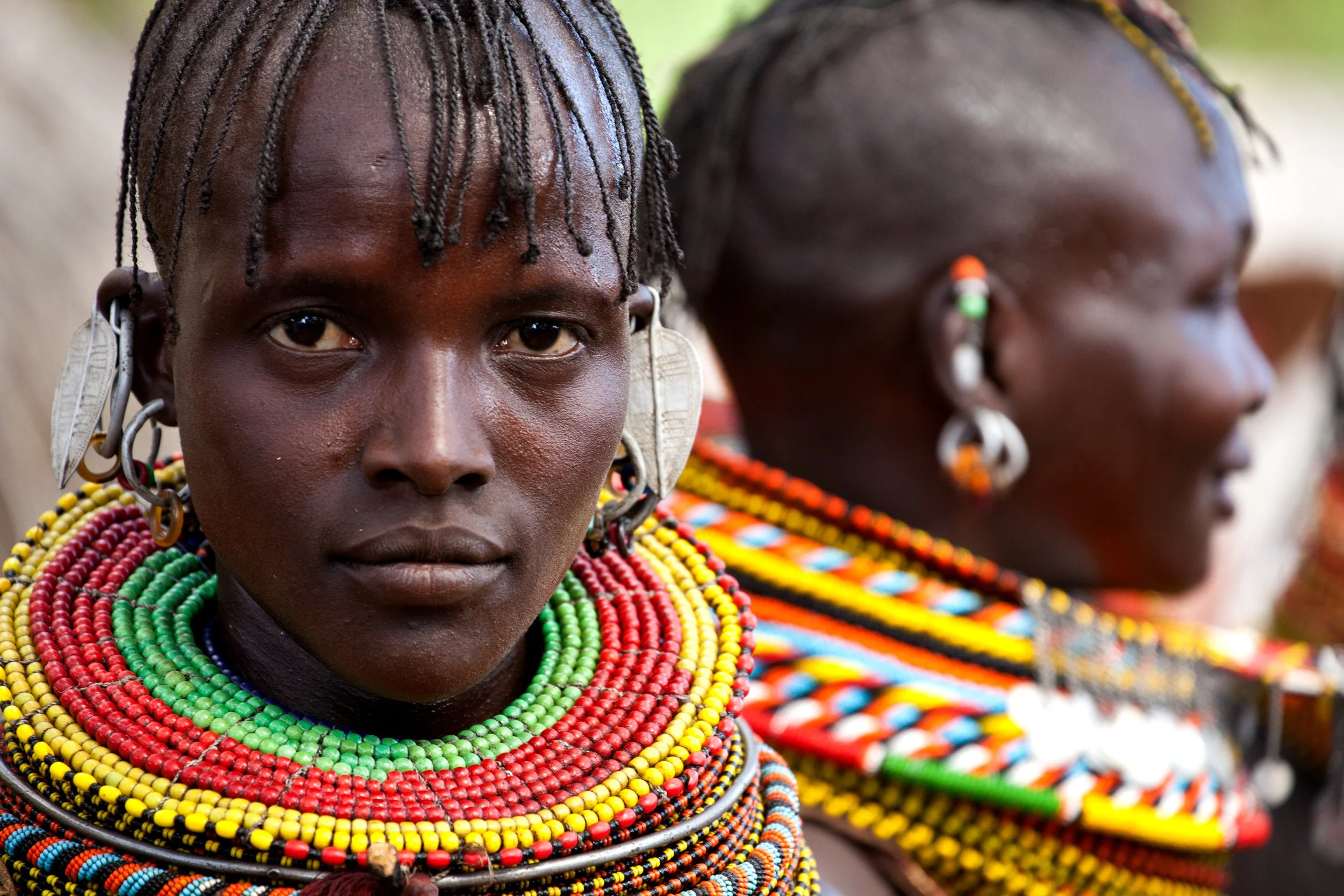 Zwei Frauen aus Afrika tragen farbenfrohen traditionellen Schmuck und Kleidung.
