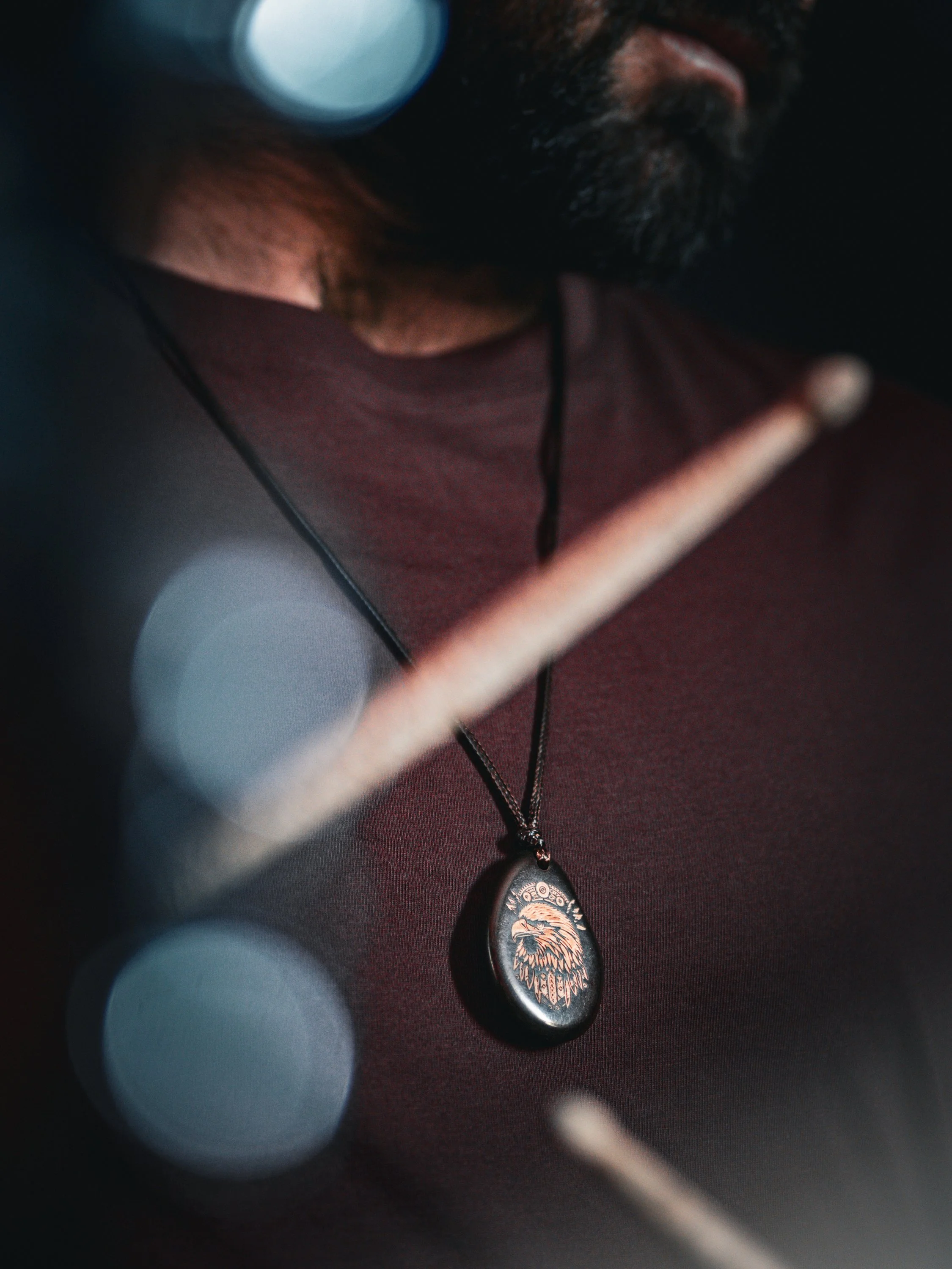 Nahaufnahme eines Mannes mit dunklem Bart, der eine schwarze Kette mit Anhänger trägt, auf dem ein Adler abgebildet ist, während er ein Musikinstrument spielt.