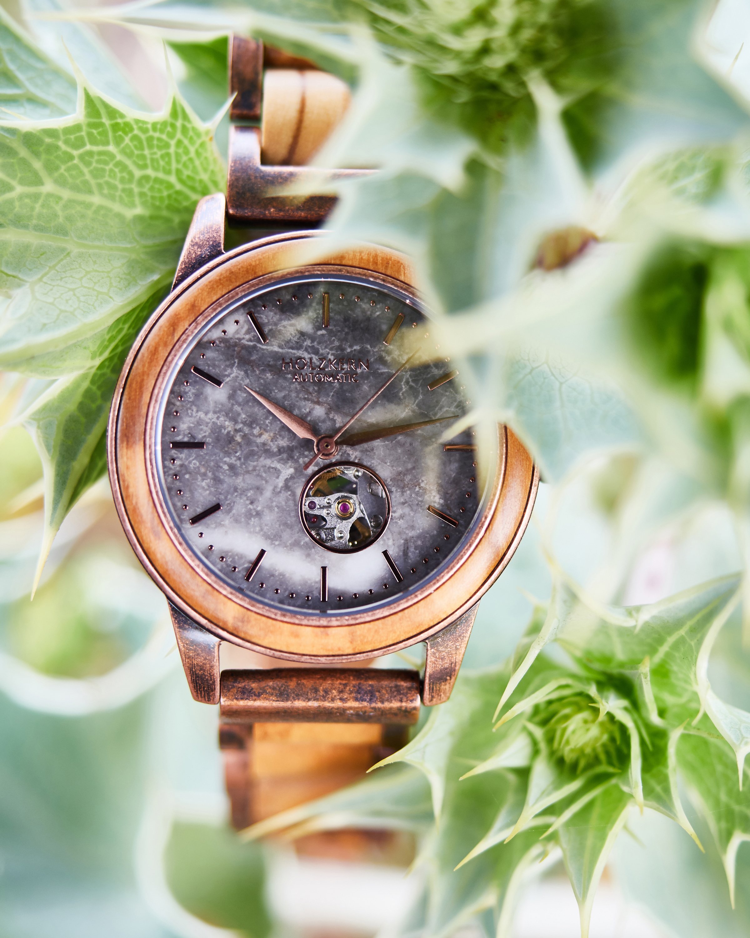 Eine Armbanduhr mit einem Holzgehäuse und Lederarmband, umgeben von grünen Stechpalmenblättern.
