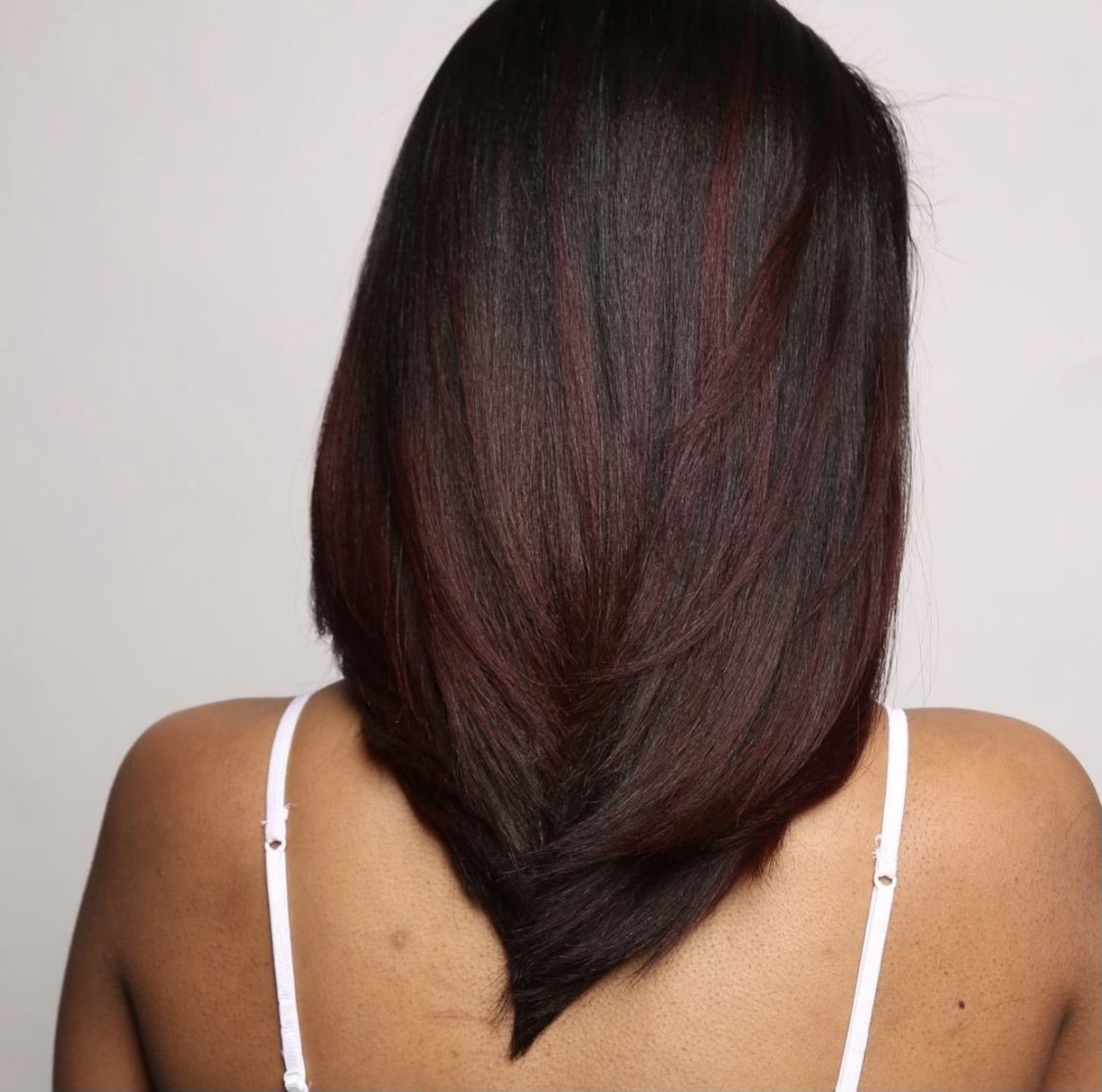 Back view of a woman with straight, shoulder-length hair dyed black with red highlights.