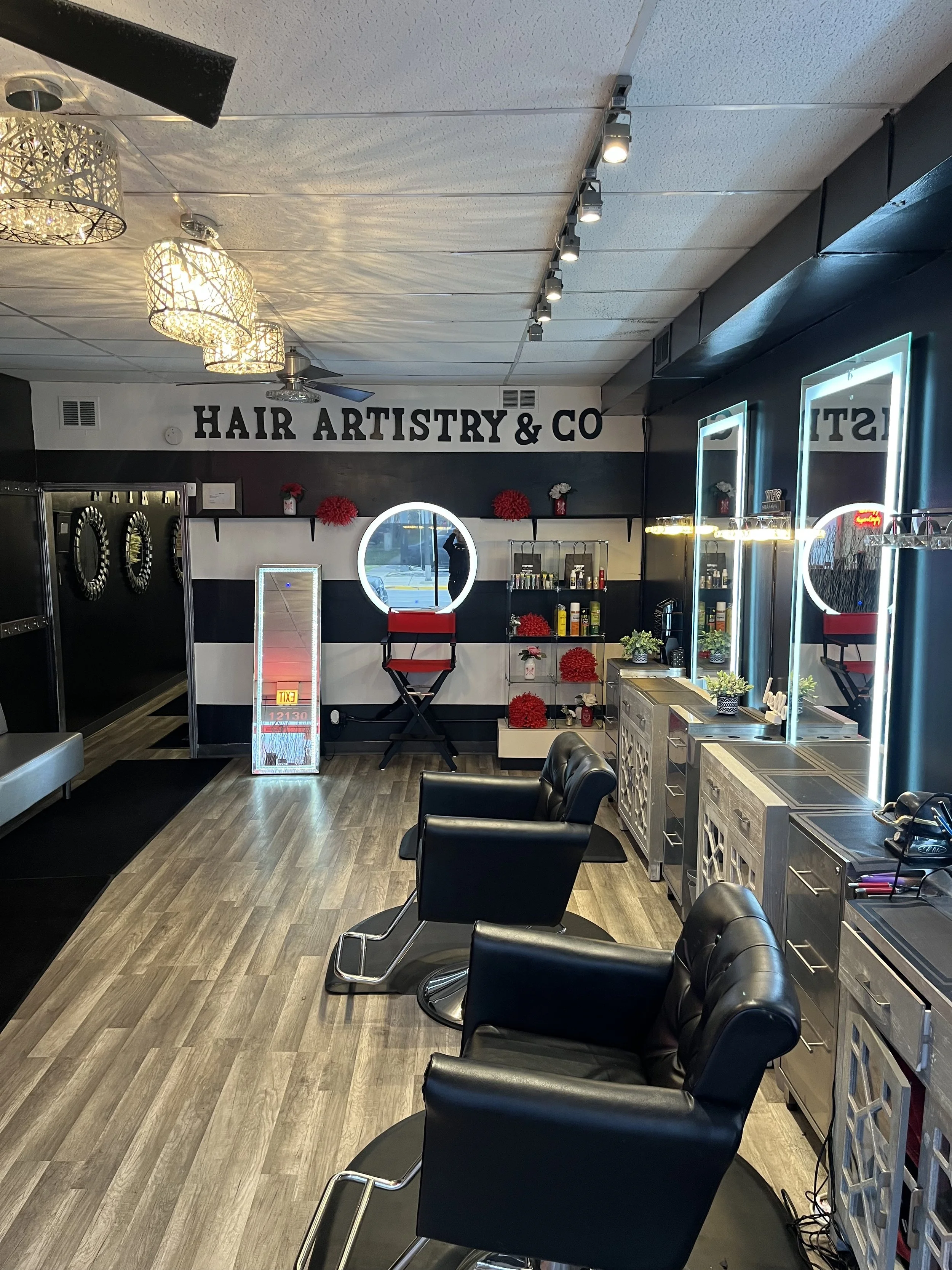 Interior of a hair salon with black and white walls, hair styling chairs, mirrors with neon lights, and shelves with hair products.