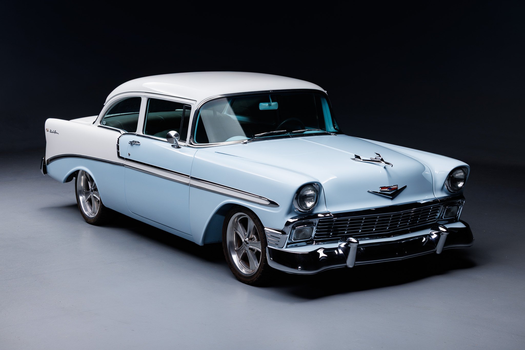 A vintage light blue Chevrolet car with chrome accents, parked on a gray surface against a black background.