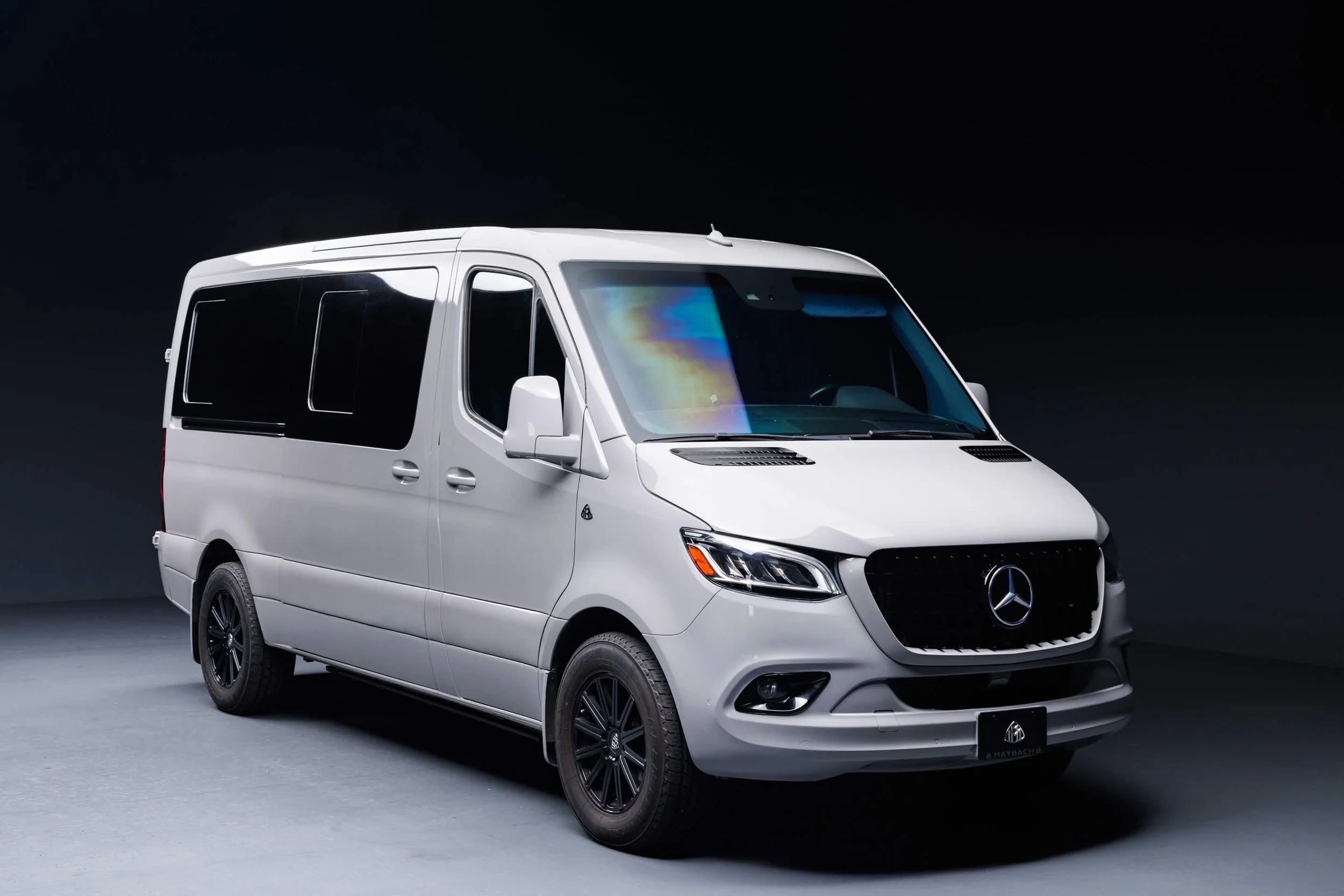 A white Mercedes-Benz van with black wheels and tinted windows, displayed against a dark background.