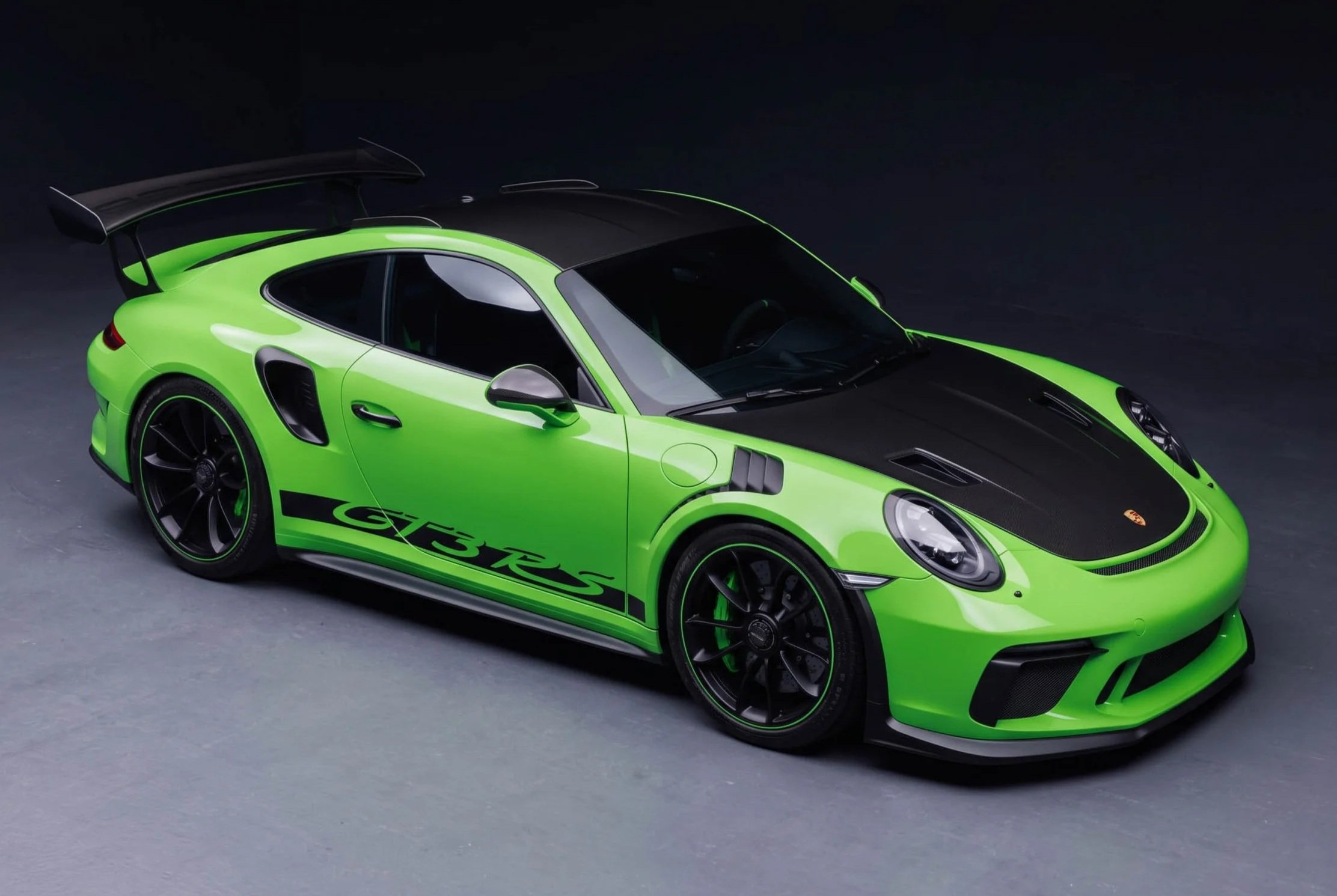Green Porsche 911 GT3 RS sports car with black accents and a large rear wing, displayed on a dark surface.
