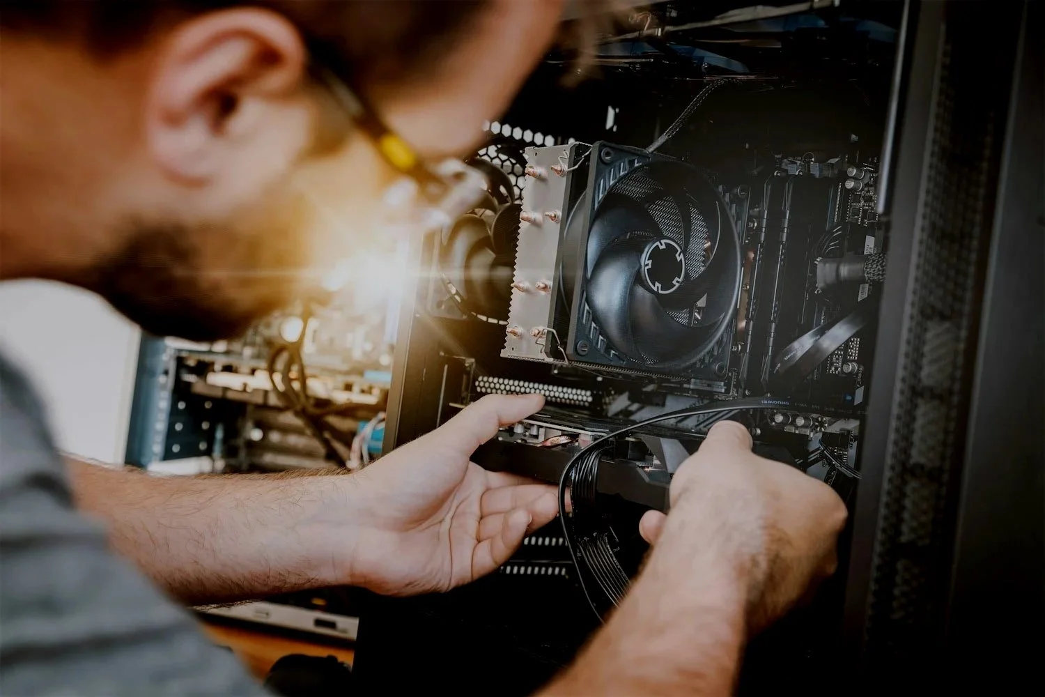 A person installing or repairing components inside a black computer tower case, with visible CPU cooler, motherboard, and cables.