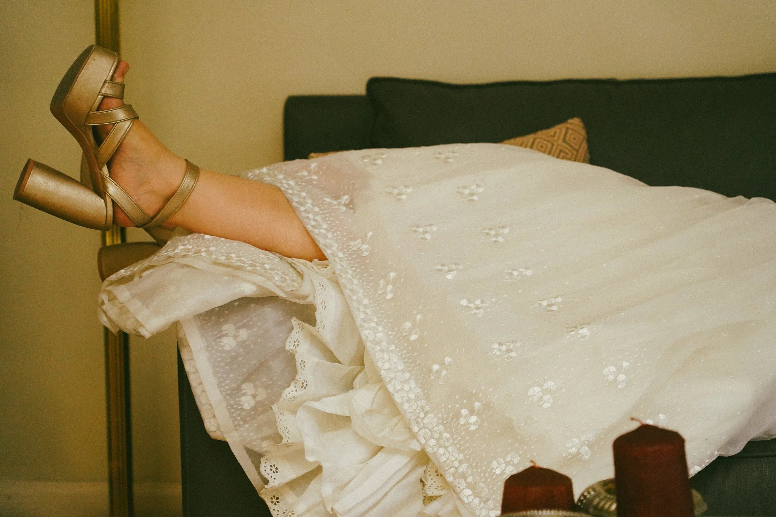 Persona acostada en una cama con vestido blanco y tacones dorados.