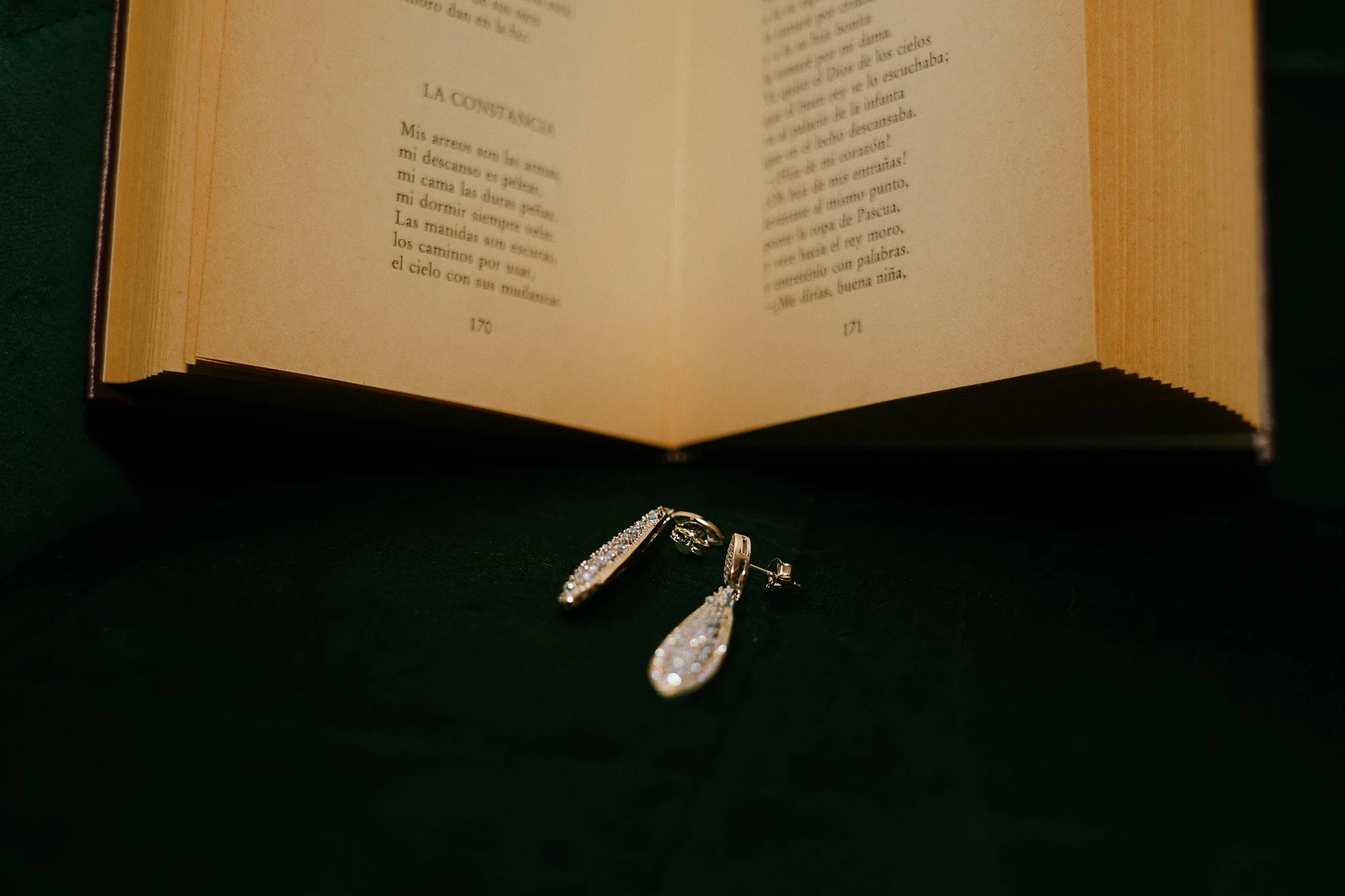 Un libro abierto en español con un par de aretes de perlas y cristales en primer plano, sobre un fondo oscuro.