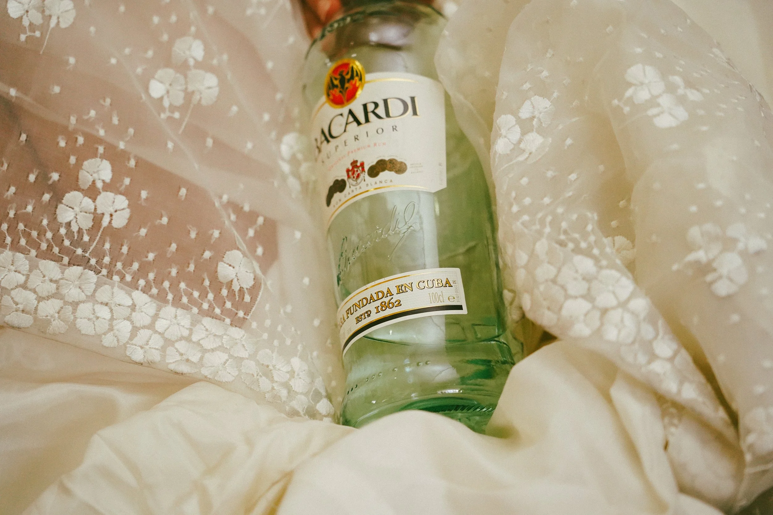 Botella de ron Bacardi en medio de un fondo de tela blanca con detalles de encaje.