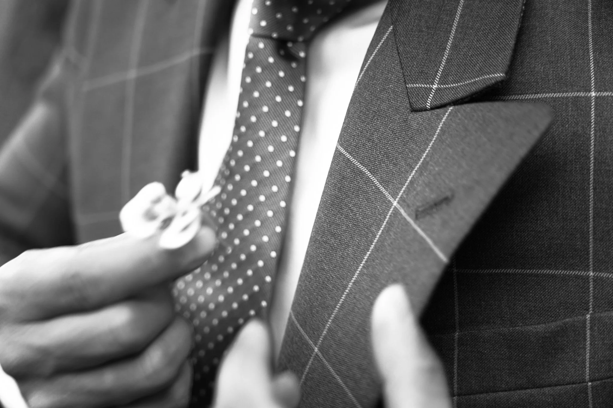 Persona ajustándose la corbata de un traje gris con patrón de cuadros finos.