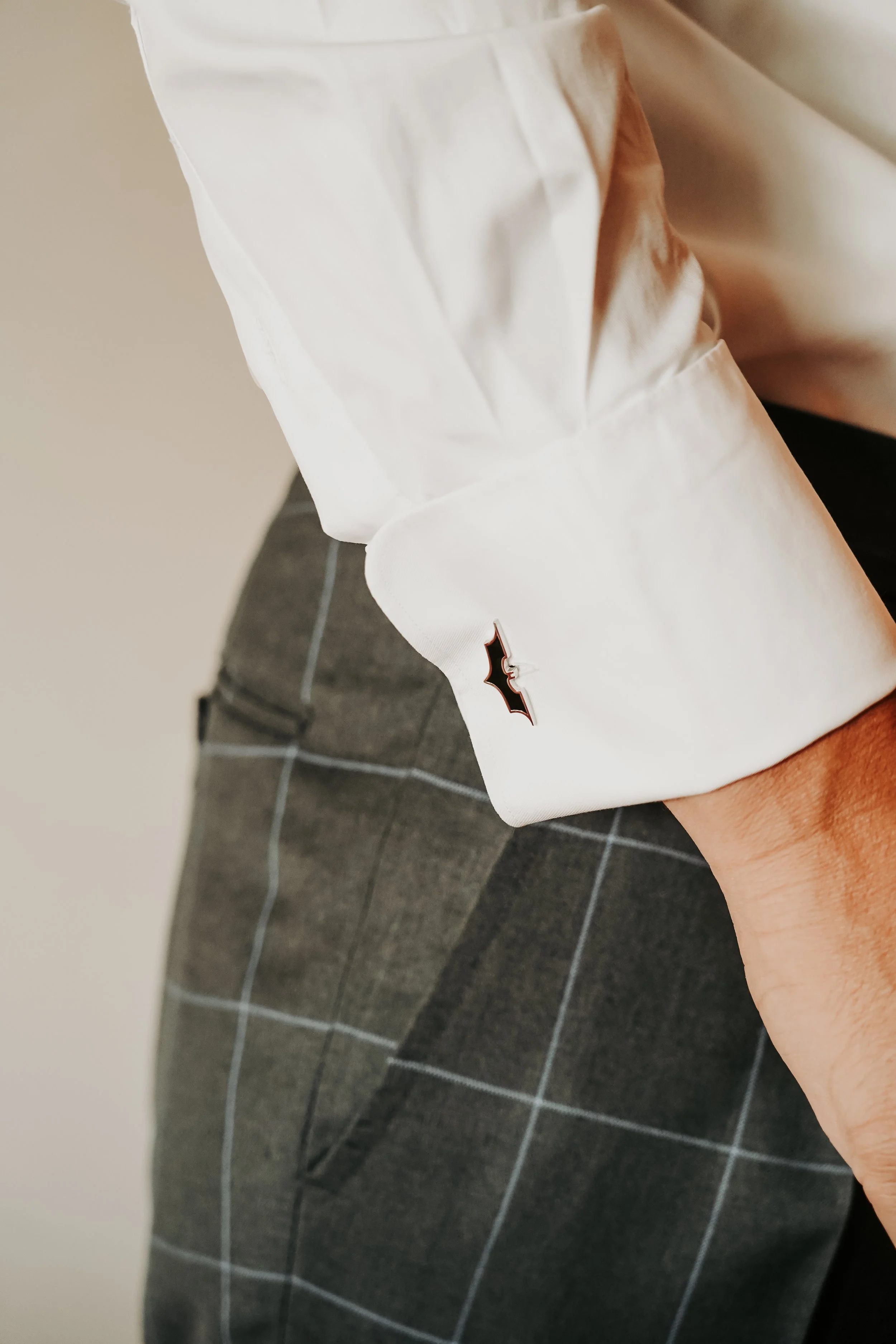 Muñeca de camisa blanca con pin de murciélago, pantalones de cuadros grises.