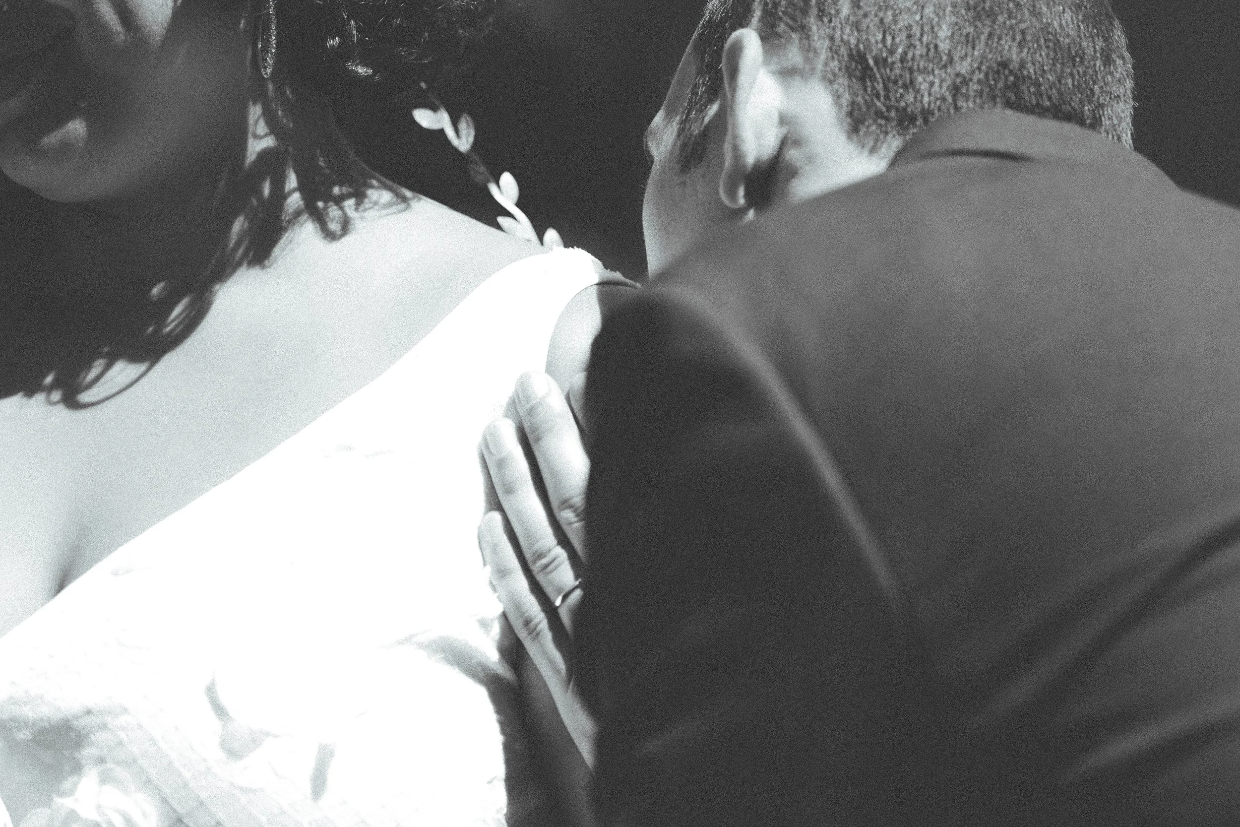Una pareja abraza, la mujer con vestido blanco y el hombre con saco oscuro, en un momento emotivo.