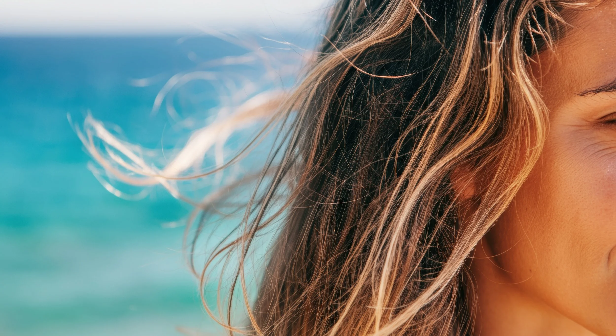 Close-up of a woman's face and hair with the ocean in the background.