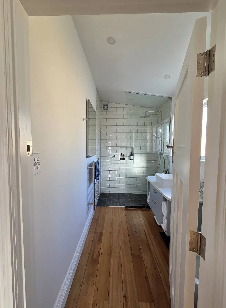 Bright modern white bathroom interior with shower, sink, and wooden floor.