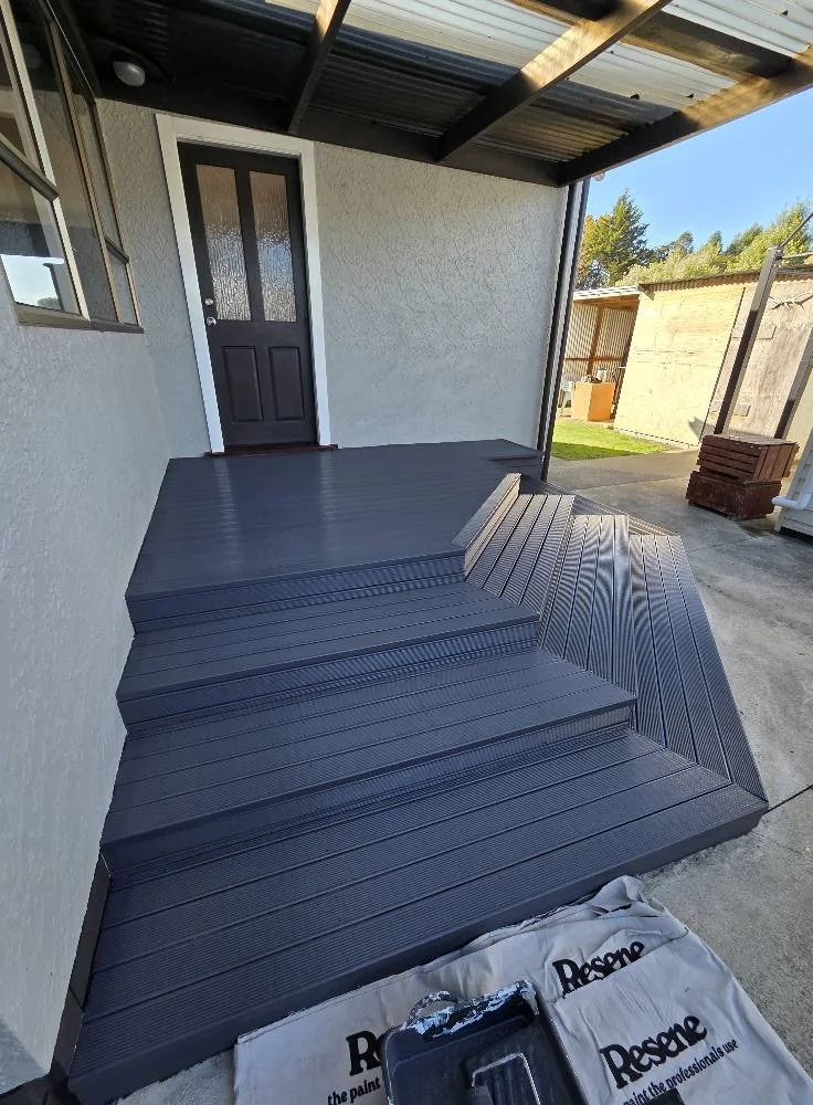 Freshly installed grey composite deck stairs leading up to a back door on a house with a covered porch.
