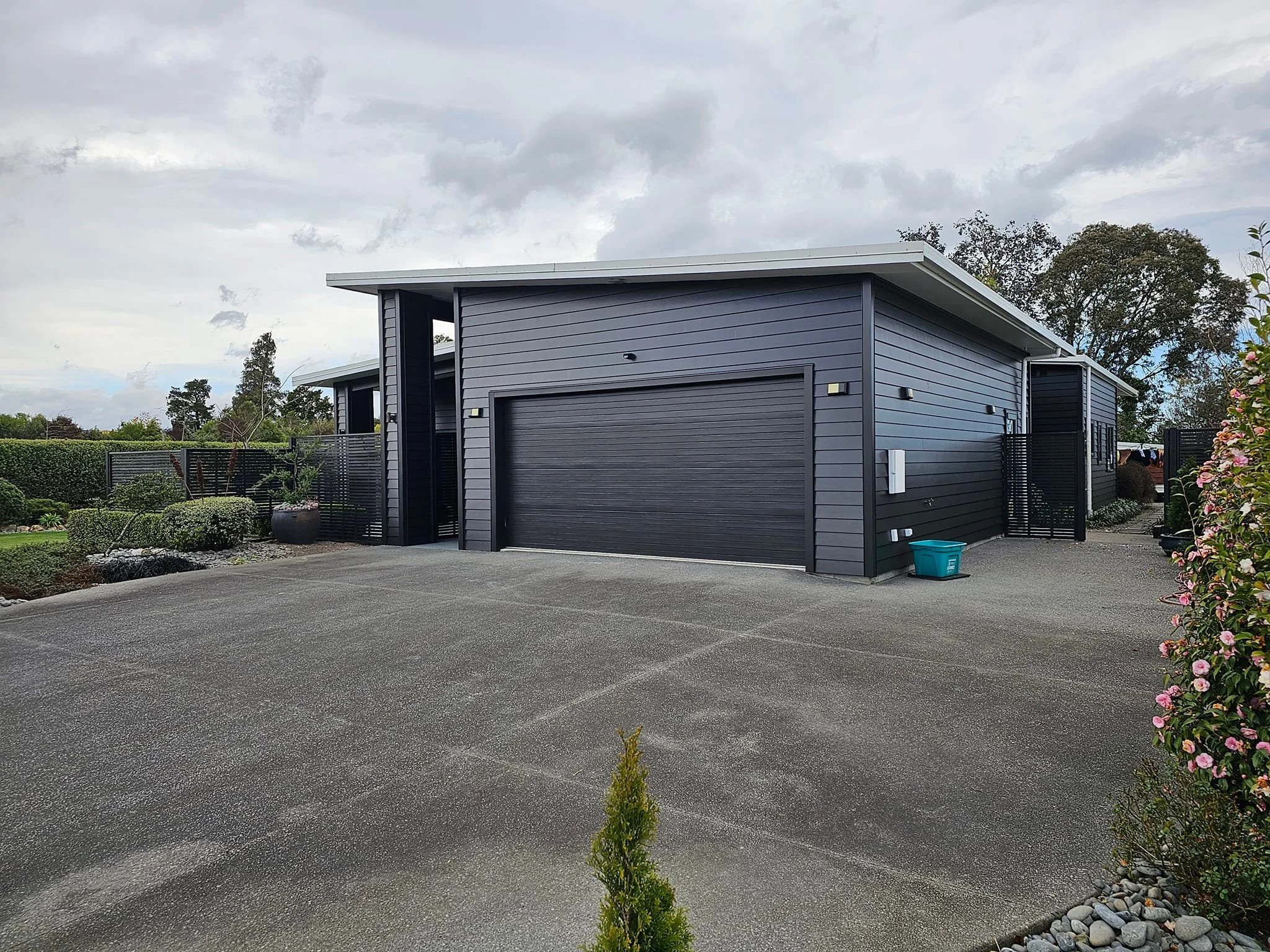 Garage and driveway of dark grey modern house under cloudy sky.