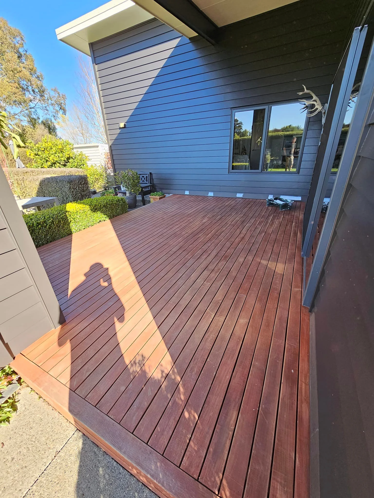Stained wooden deck at side of dark grey modern house on a sunny day.