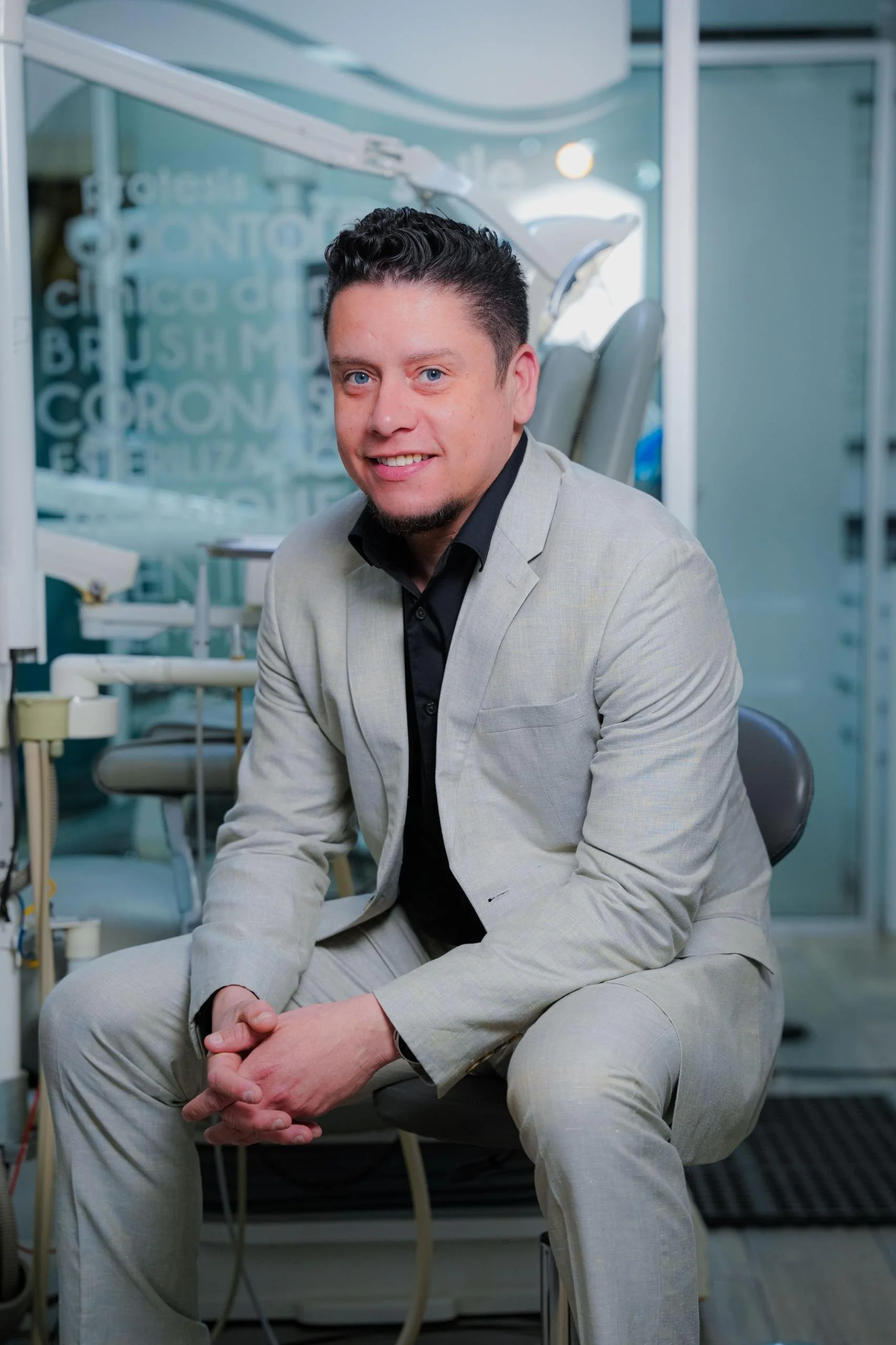 Hombre con traje gris sentado en una clínica dental, con equipos dentales y palabras relacionadas en el fondo.