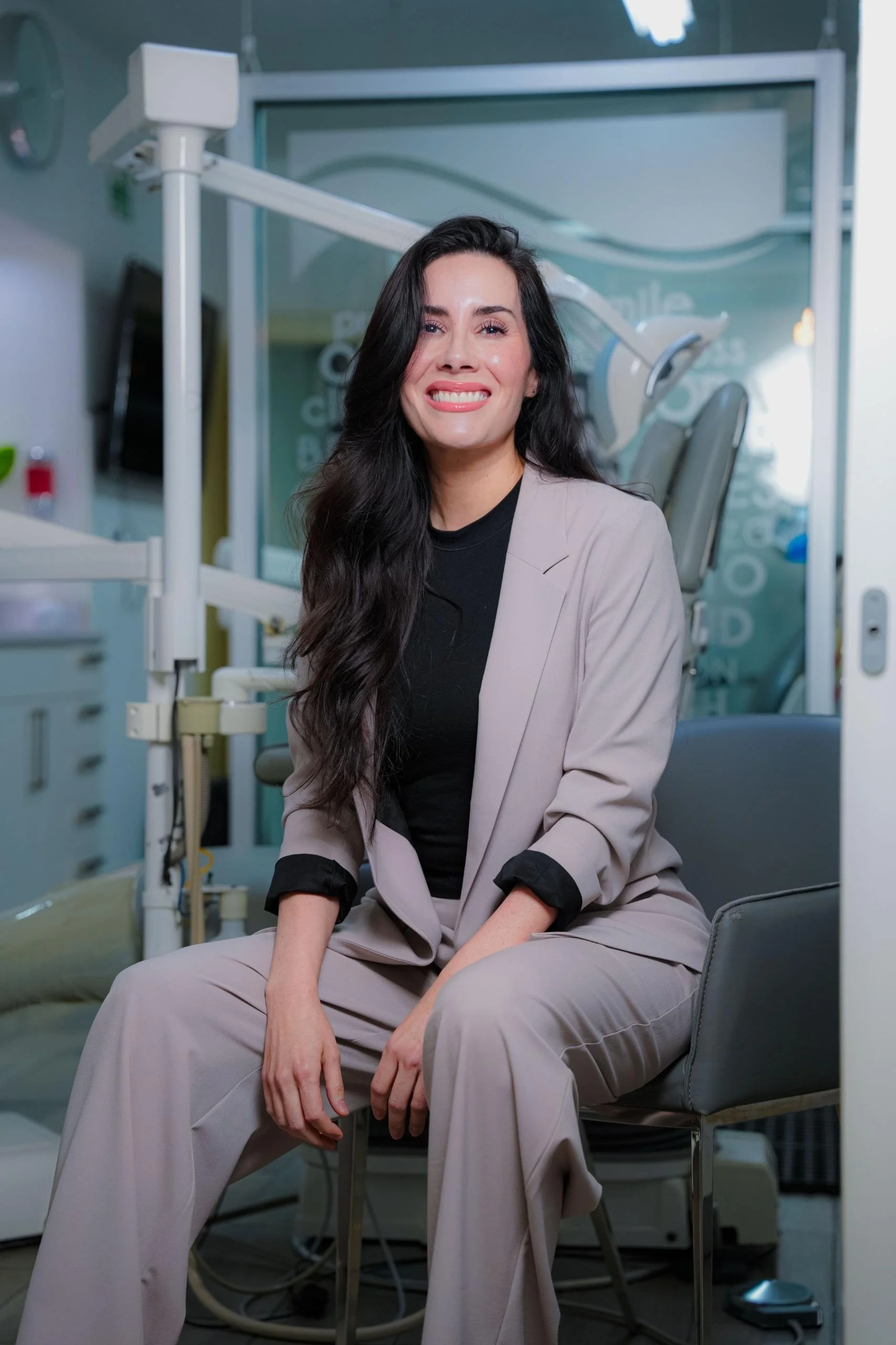 Mujer sentada en una clínica dental, sonriendo, con equipo dental en el fondo.