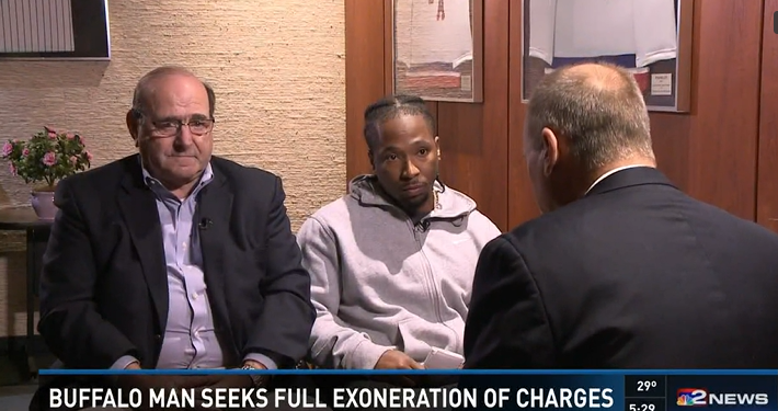 Three men sitting in a room during an interview or conversation, with a news headline about a Buffalo man seeking exoneration of charges at the bottom of the screen.