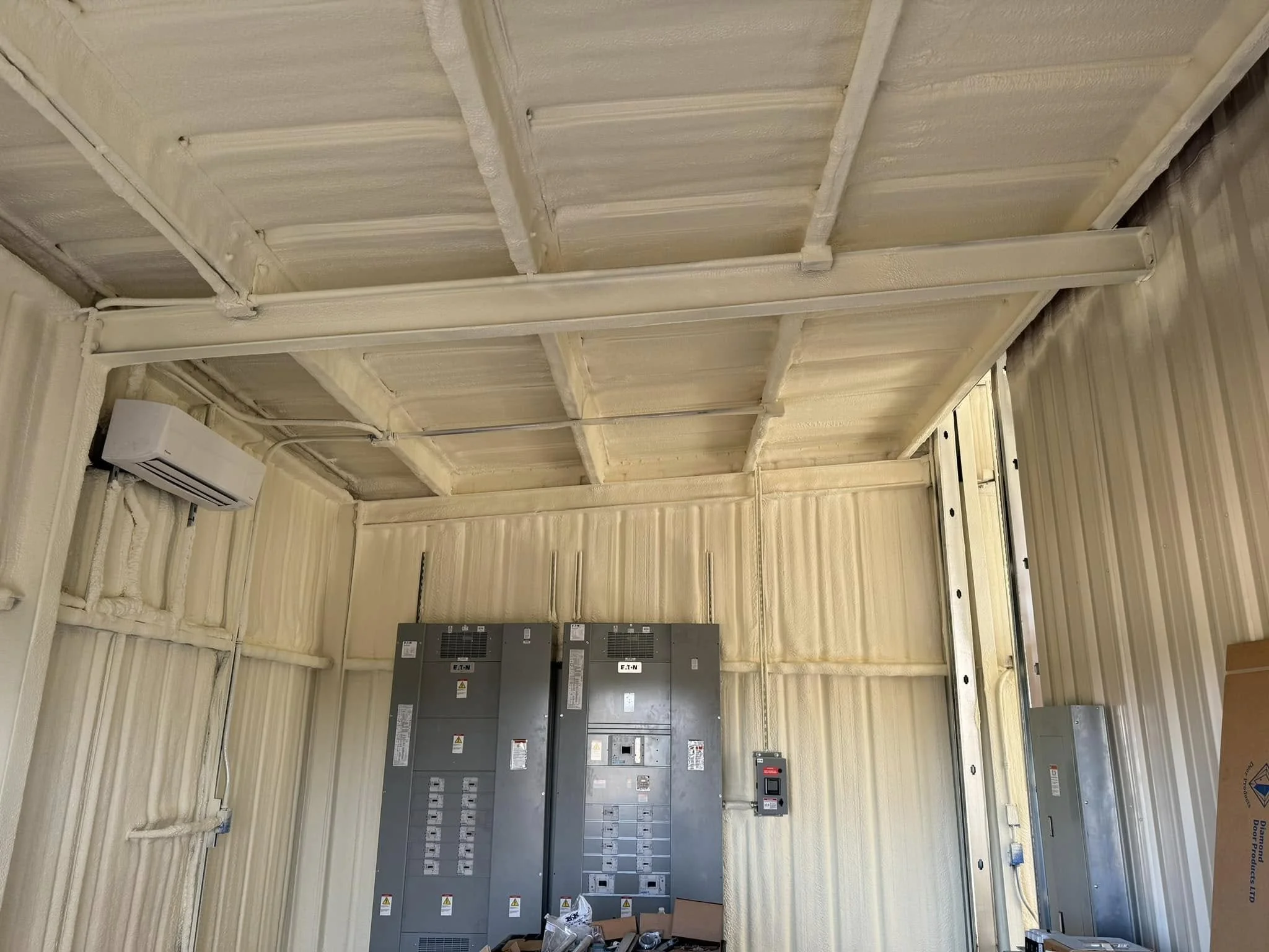 Interior view of a room with electrical panels on the wall, an air conditioning unit, and insulation on the ceiling and walls.