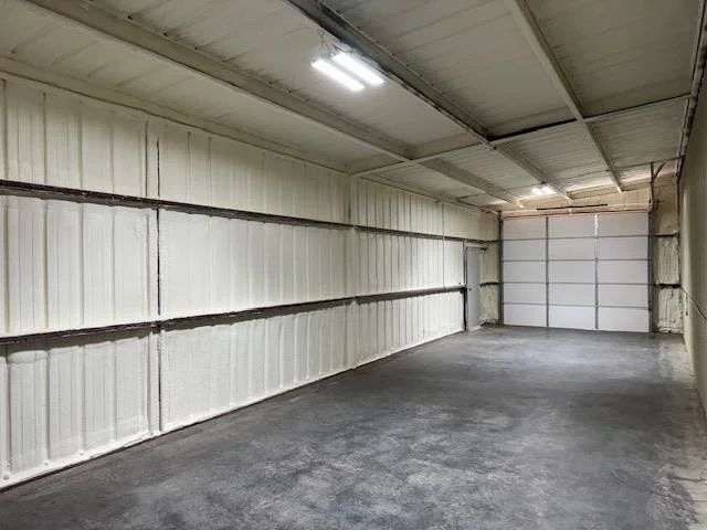 Empty garage with white walls, concrete floor, and a metal rolling door at the far end.