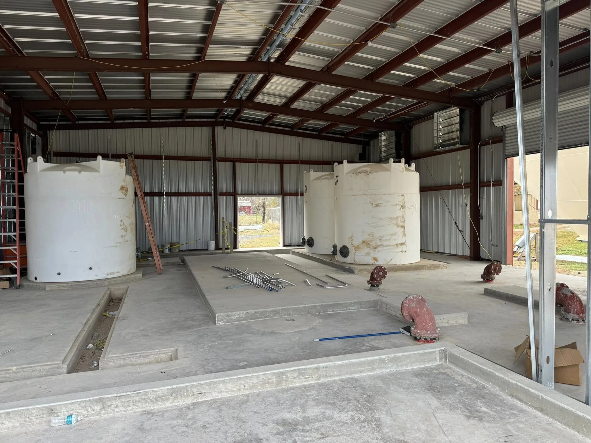 Construction site inside a building with three large white tanks, exposed metal beams, and unfinished concrete floor.