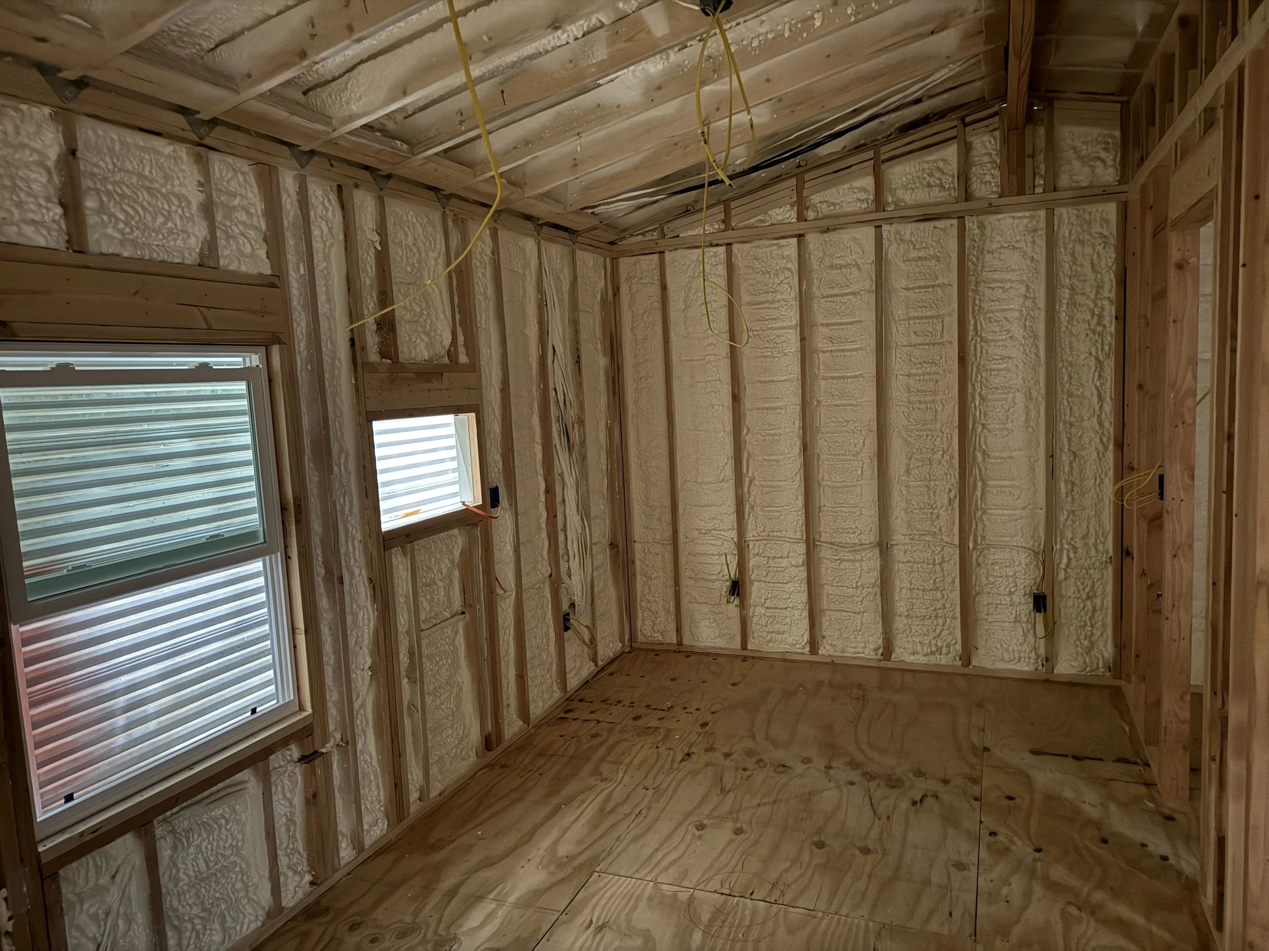 An unfinished room with wooden framing, insulation, and two windows