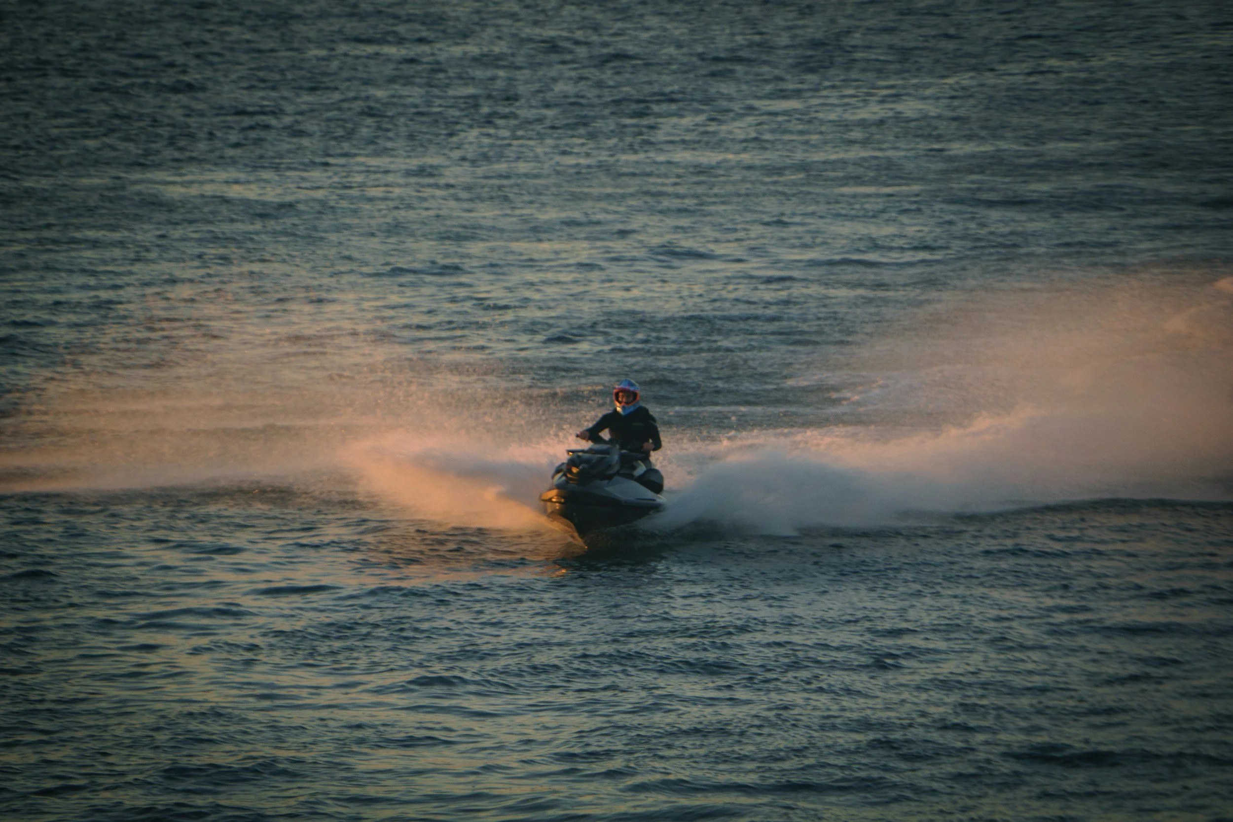 Person riding a jet ski on the water at sunset.