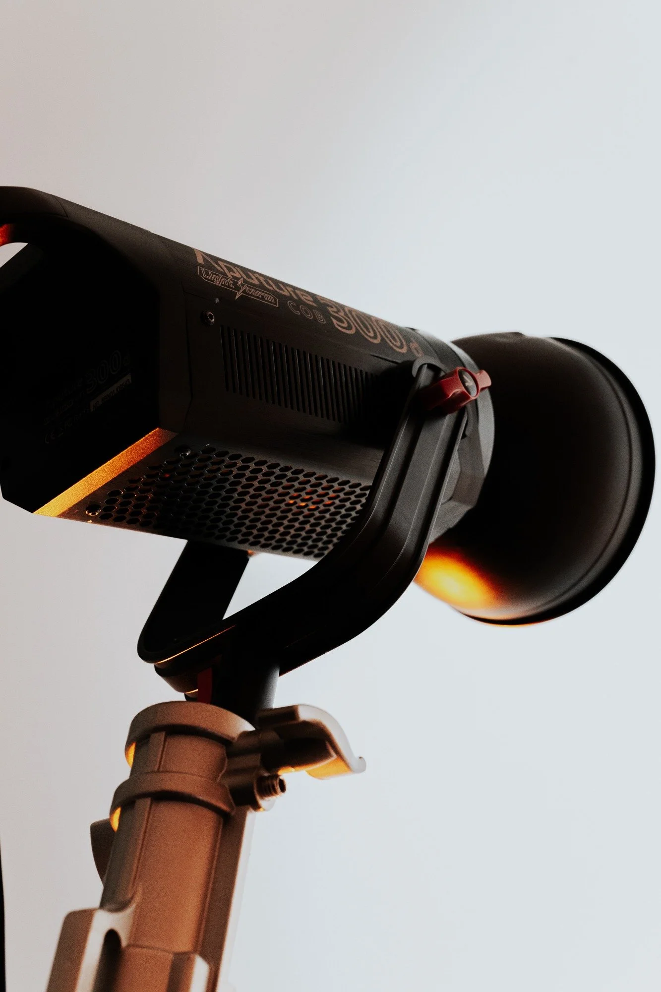A professional stage or studio light mounted on a stand, illuminating a plain white wall.