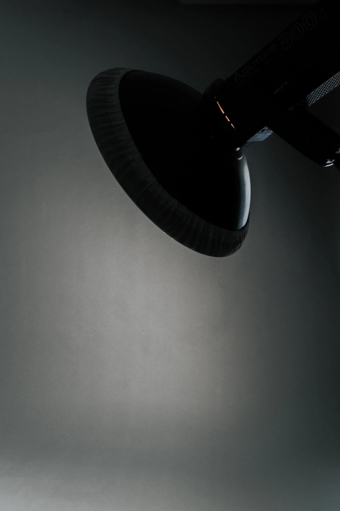 A close-up of a modern, black desk lamp with a circular, textured shade against a plain gray background.