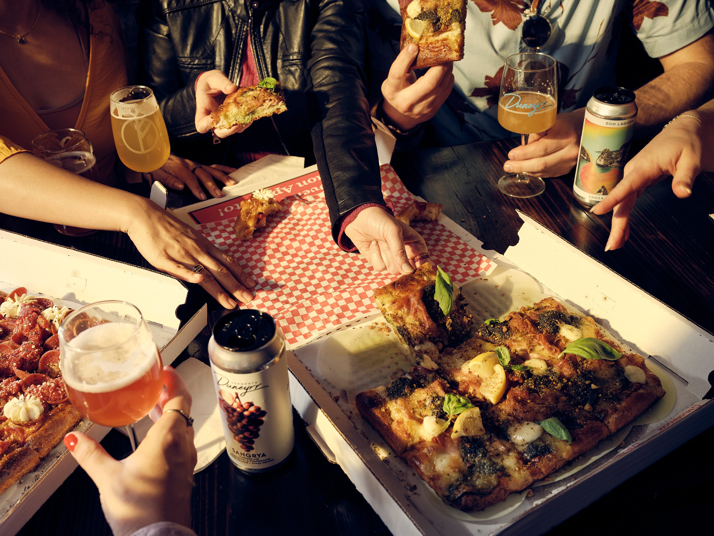 Group of people sharing pizza and drinks at a table at a birthday party at Tethered Events