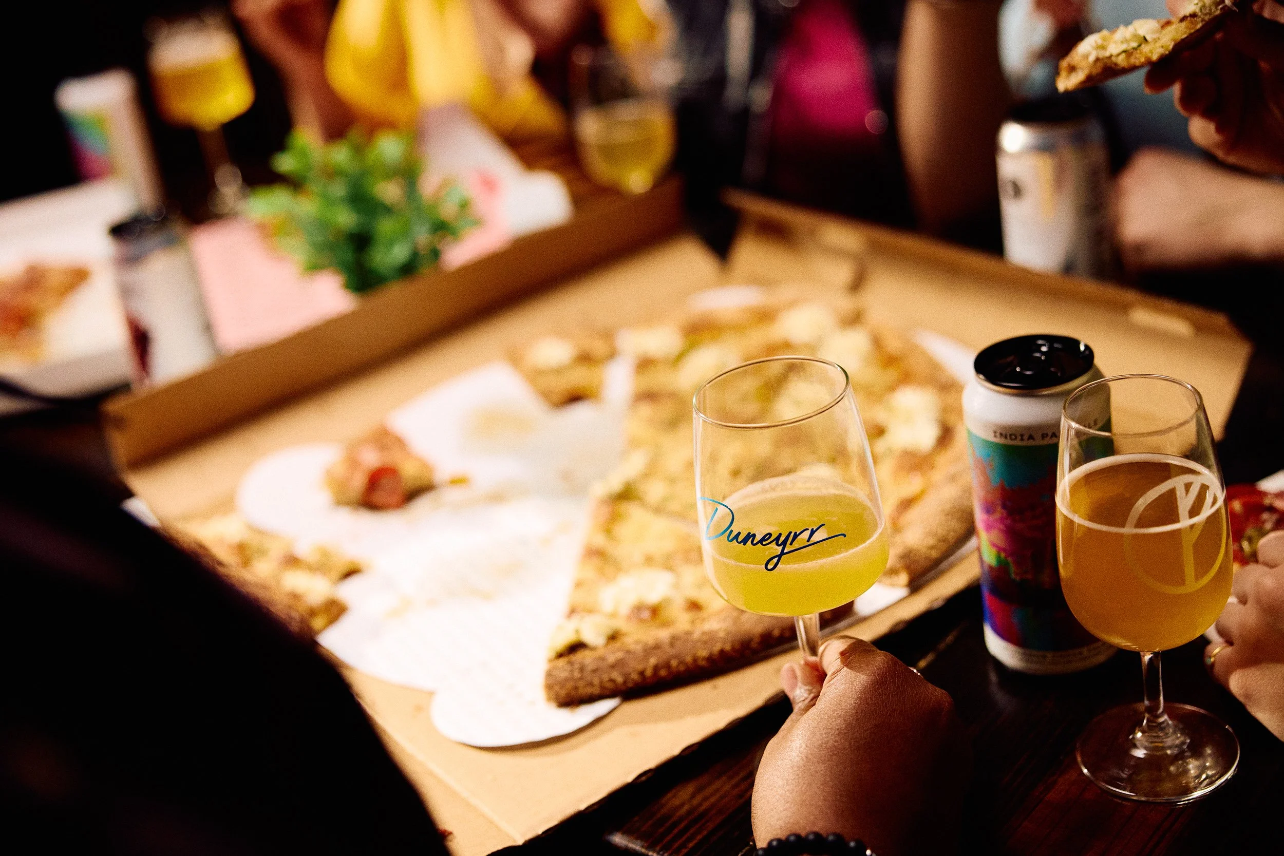 People enjoying pizza and drinks at a social gathering, with two glasses of light-colored beverage and a pizza box on the table at Tethered Events Chicago