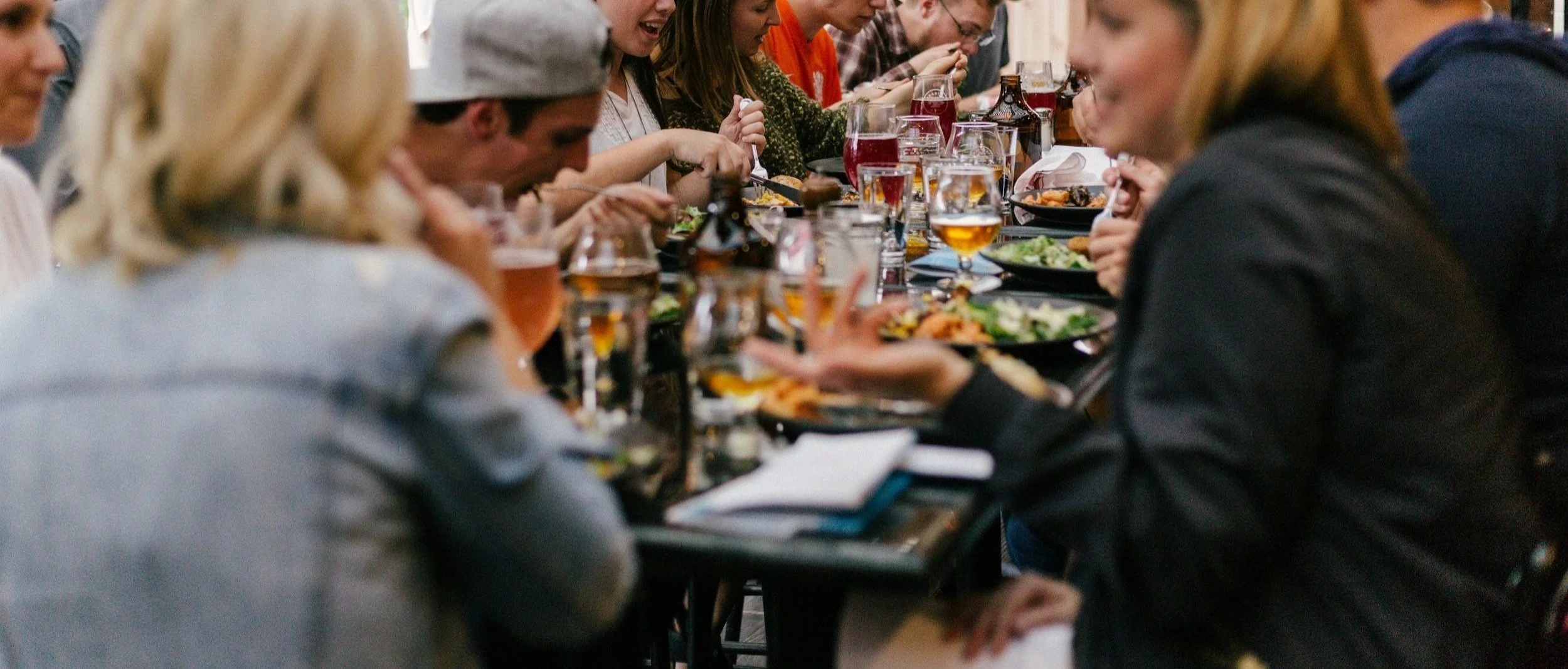 People sitting at a long dining table eating a meal and drinking beverages in a social gathering at Tethered Events Chicago