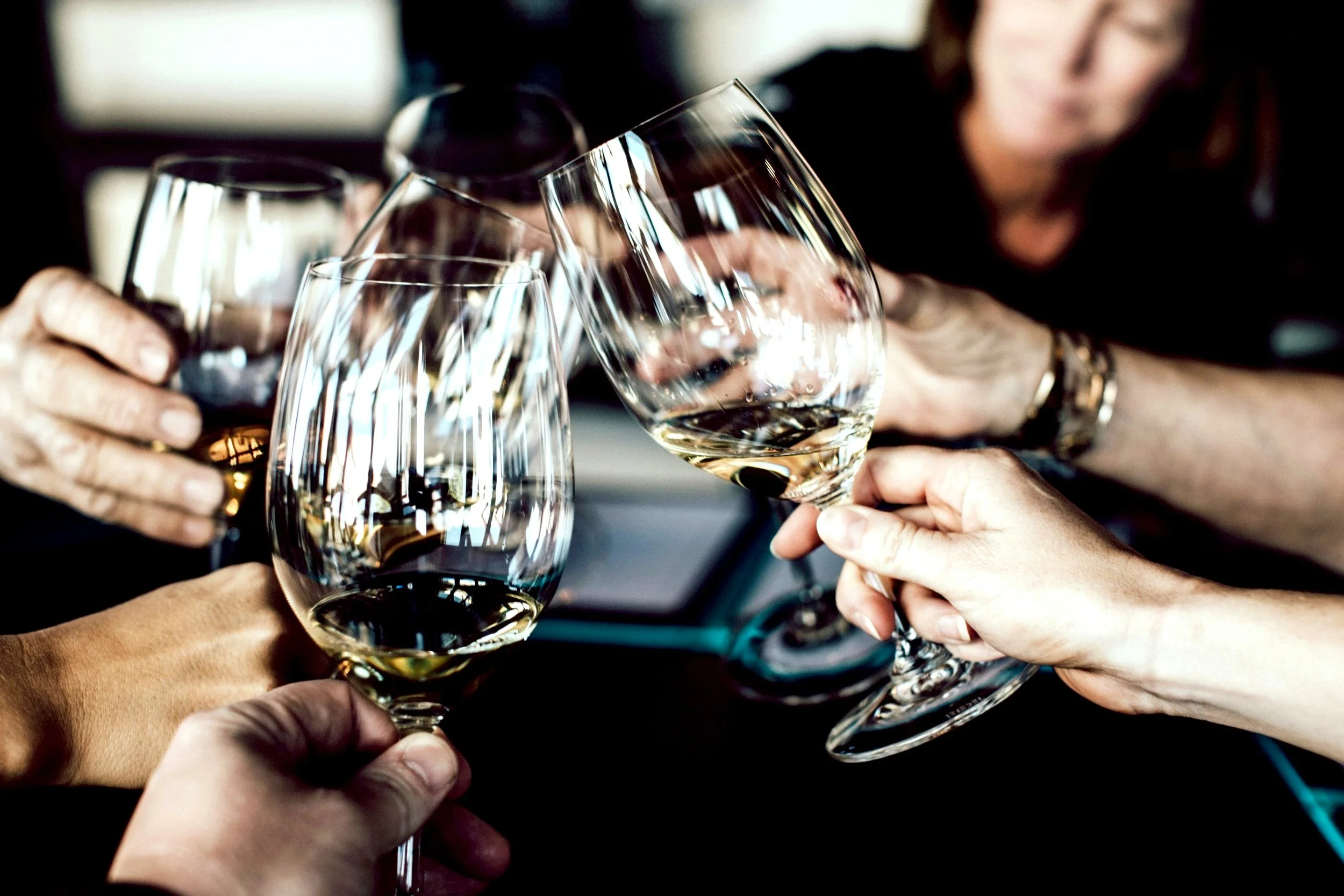 Several people holding glasses of white wine in a corporate toast celebration.