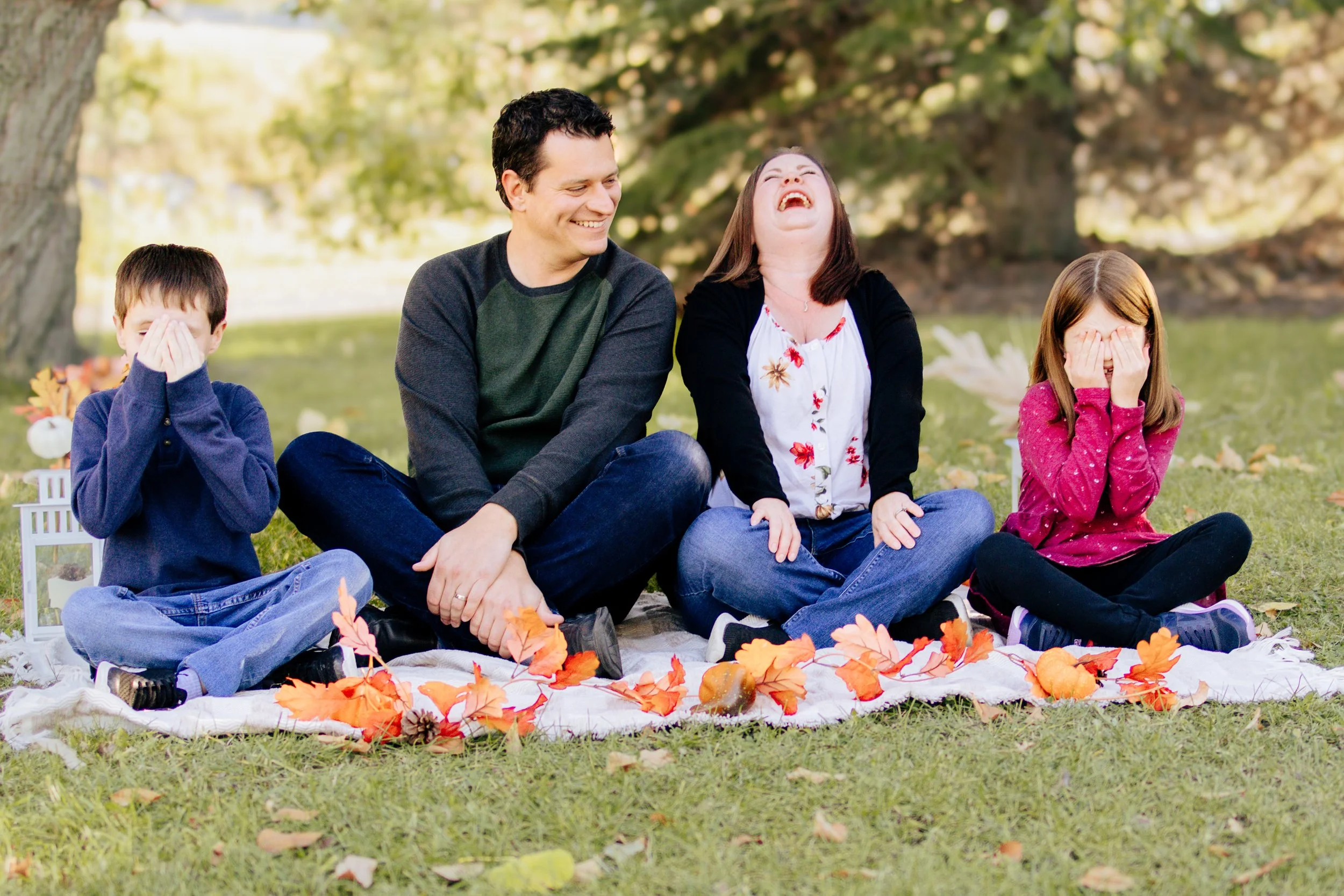 Parents and two kids sitting close together, smiling during their outdoor family session.