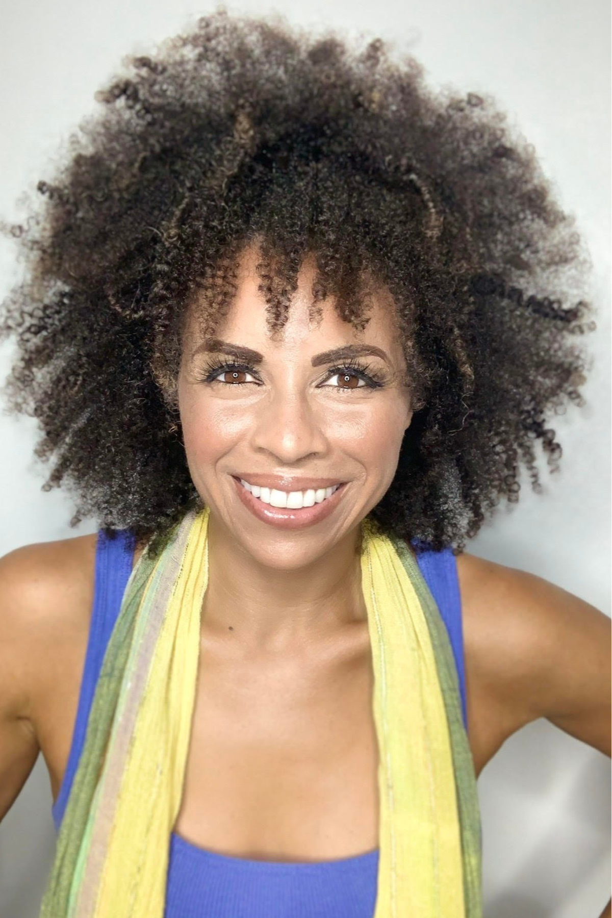 A woman with curly hair wearing a red blazer, smiling against a red background.