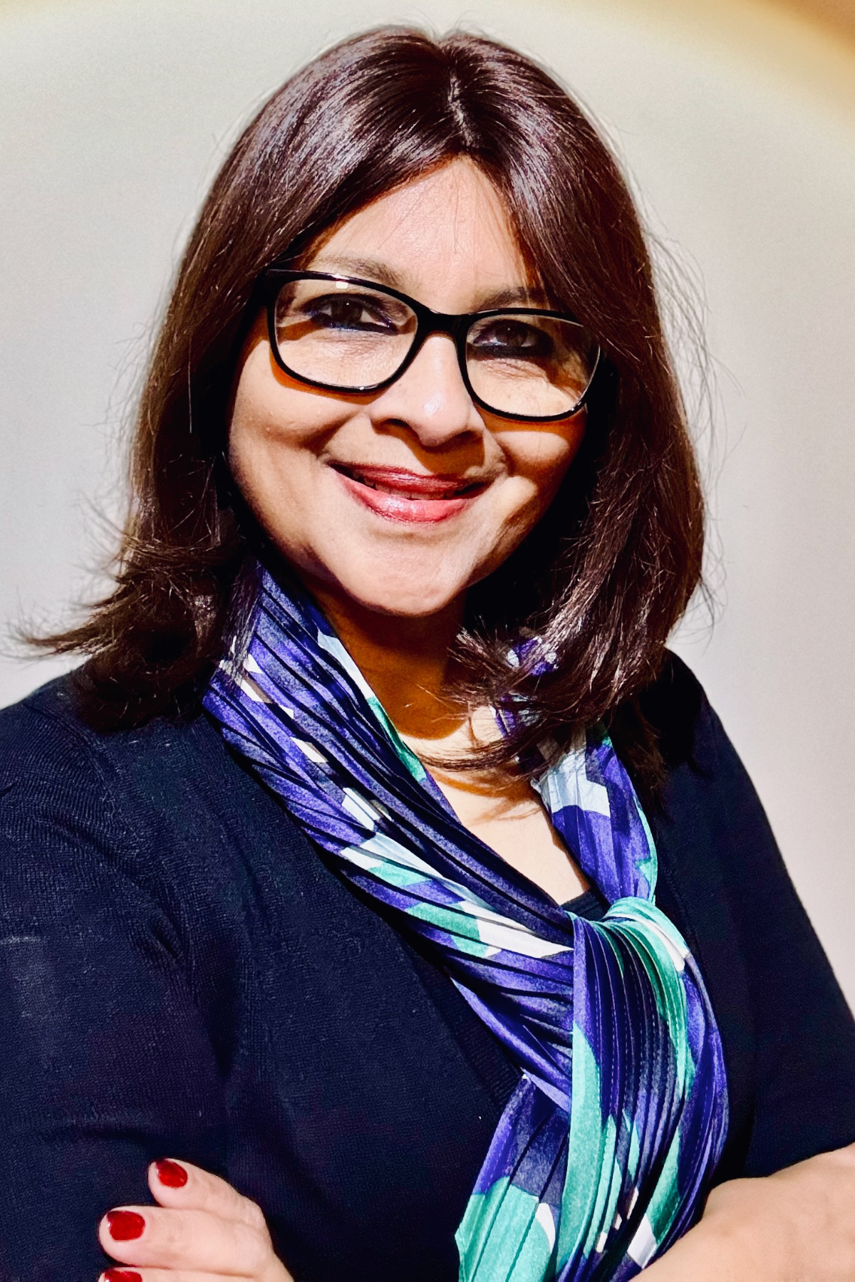 Black and white photo of a woman with curly hair, glasses, and a broad smile, standing against a plain background.