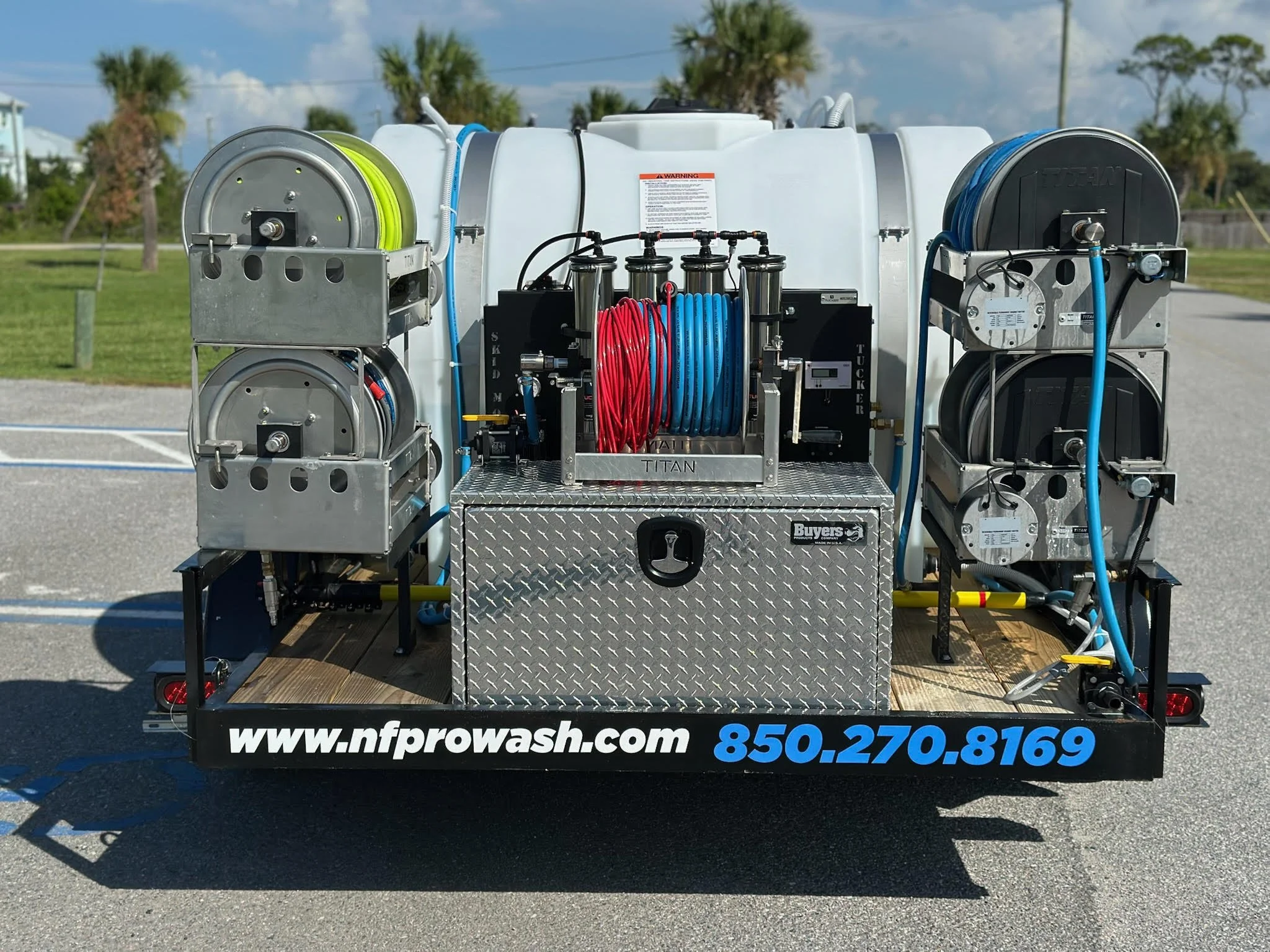 Mobile car wash equipment with hoses, reels, and a water tank on a trailer, parked outdoors.
