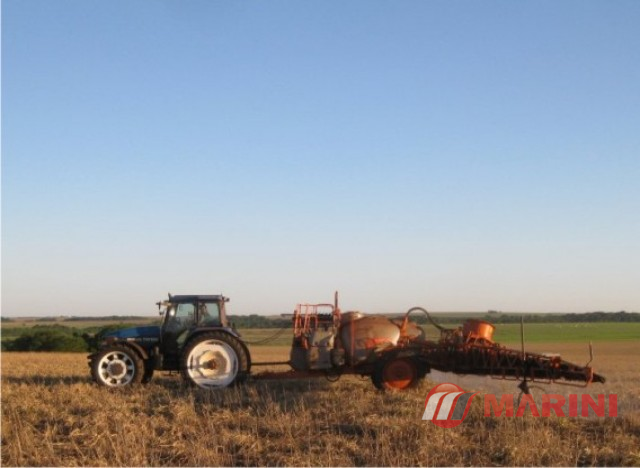 Trator em um campo cultivado, puxando uma máquina agrícola de pulverização