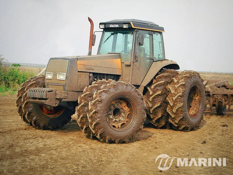 Trator agrícola de grande porte estacionado em um campo de terra.