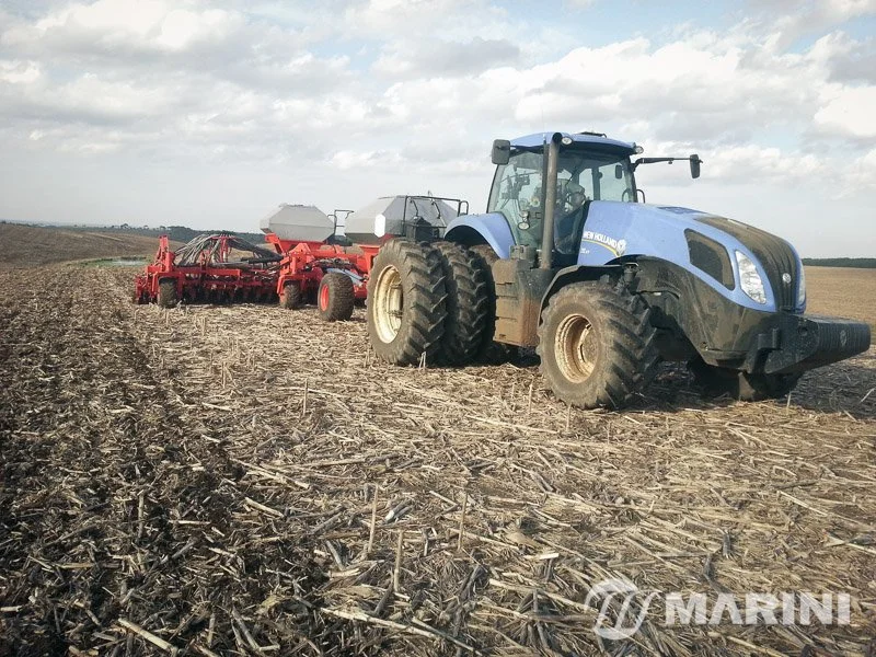 Trator agrícola azul puxando máquina de plantio em um campo de plantação