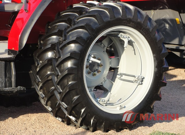 Roda de um trator agrícola com pneus grandes e profundos, parte da estrutura do trator visível ao fundo.