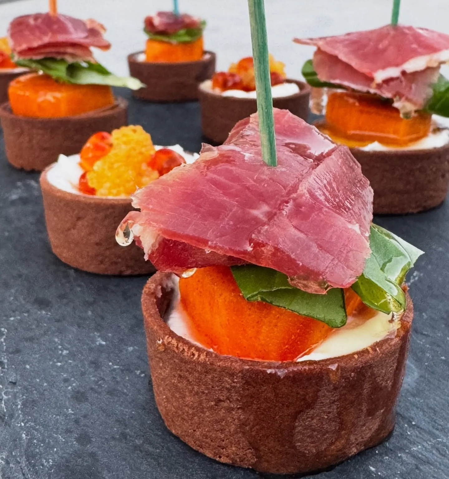 The Recipe: Kaki, Prosciutto &amp; Basil Tartlets
Ingredients:
&bull; For the Base:
&bull; 1 box pre-made mini tartlet shells (approx. 12-15 shells)
&bull; For the Filling:
&bull; 4 oz cream cheese, softened
&bull; 1/2 tsp honey (plus extra for drizz